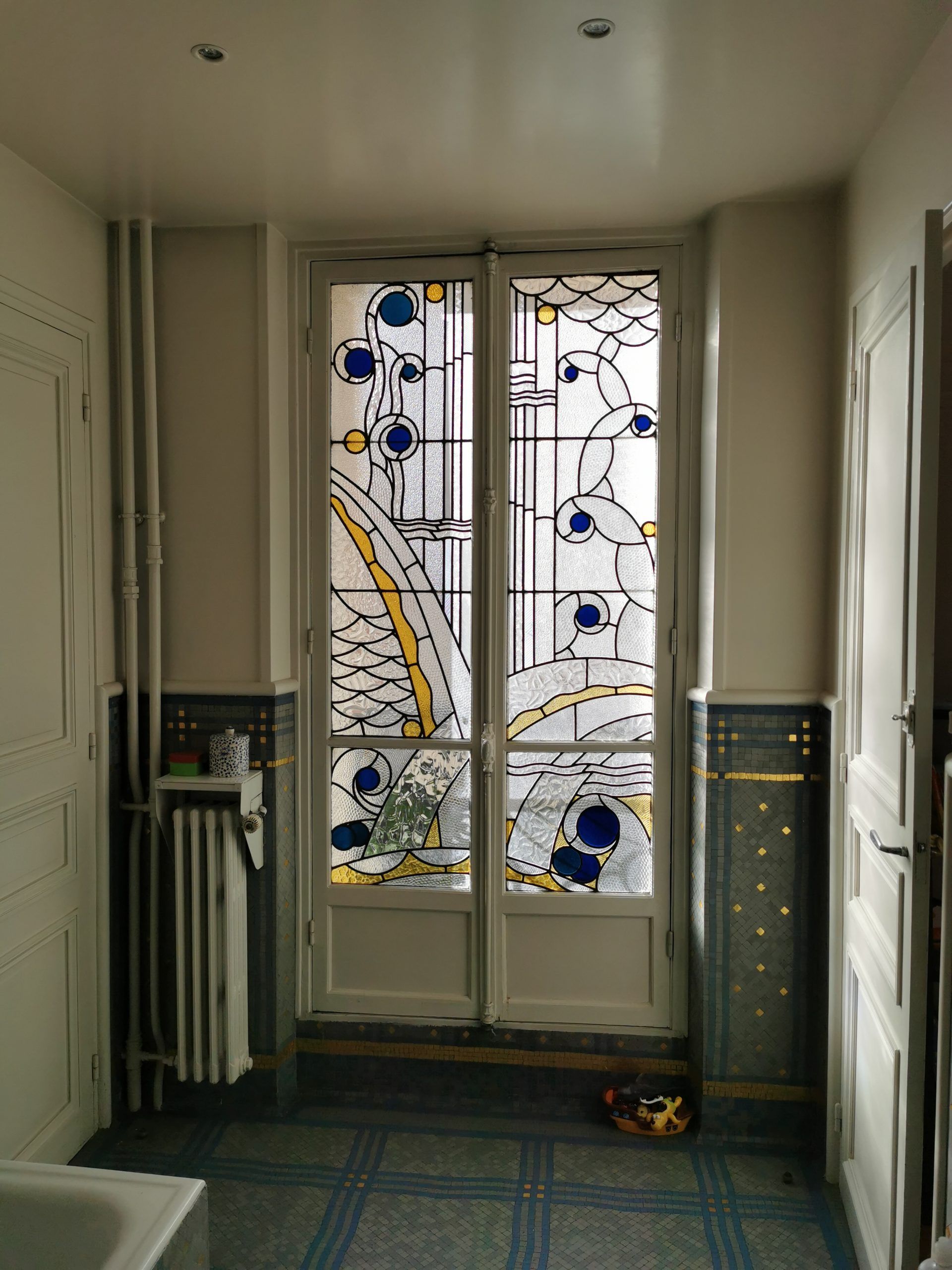 Portes doubles en vitrail avec des accents bleus et jaunes dans une pièce au sol carrelé bleu.