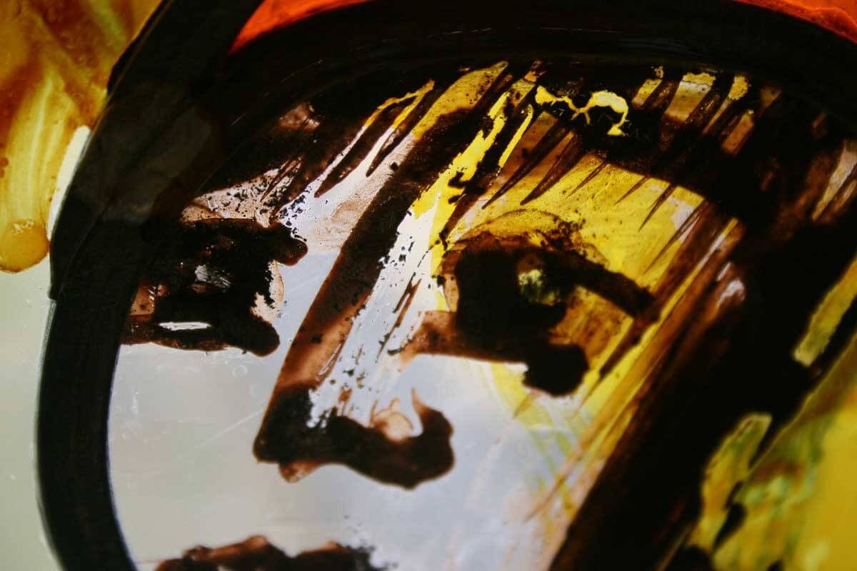 Gros plan sur un visage peint sur verre. Des coups de pinceau bruns et jaunes dessinent un œil, un nez et une bouche.