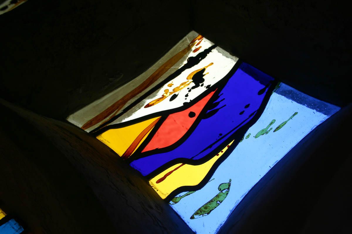 Vitrail présentant des sections jaunes, rouges, bleues et blanches ; intérieur sombre.