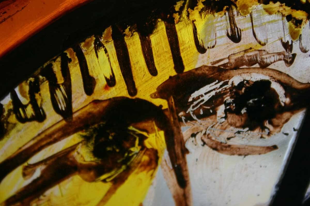 Gros plan sur un vitrail représentant un visage, dans des tons bruns et jaunes.