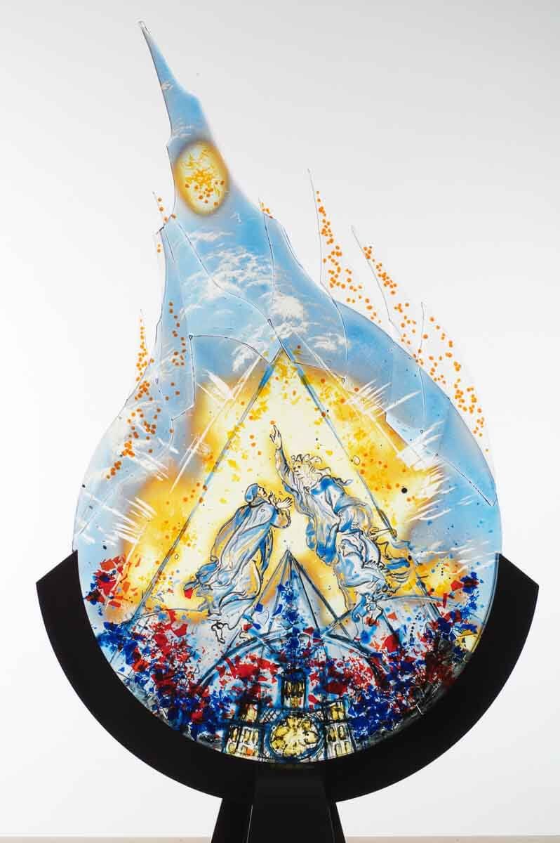 Vitrail représentant un paysage de montagne, en forme de flamme bleue, jaune et orange.