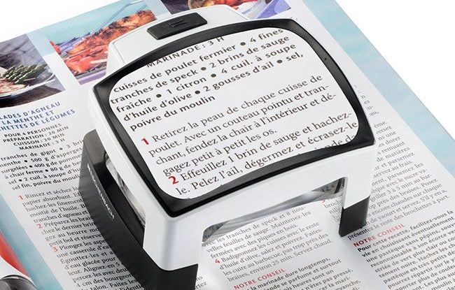 Une femme et portant des lunettes lit un livre sur un canapé.