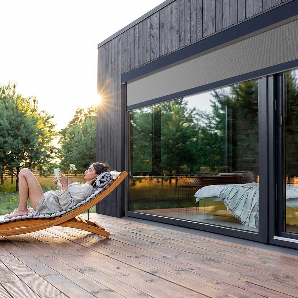 Femme lisant un livre sur un terrase en bois avec baie vitrée en arrière plan