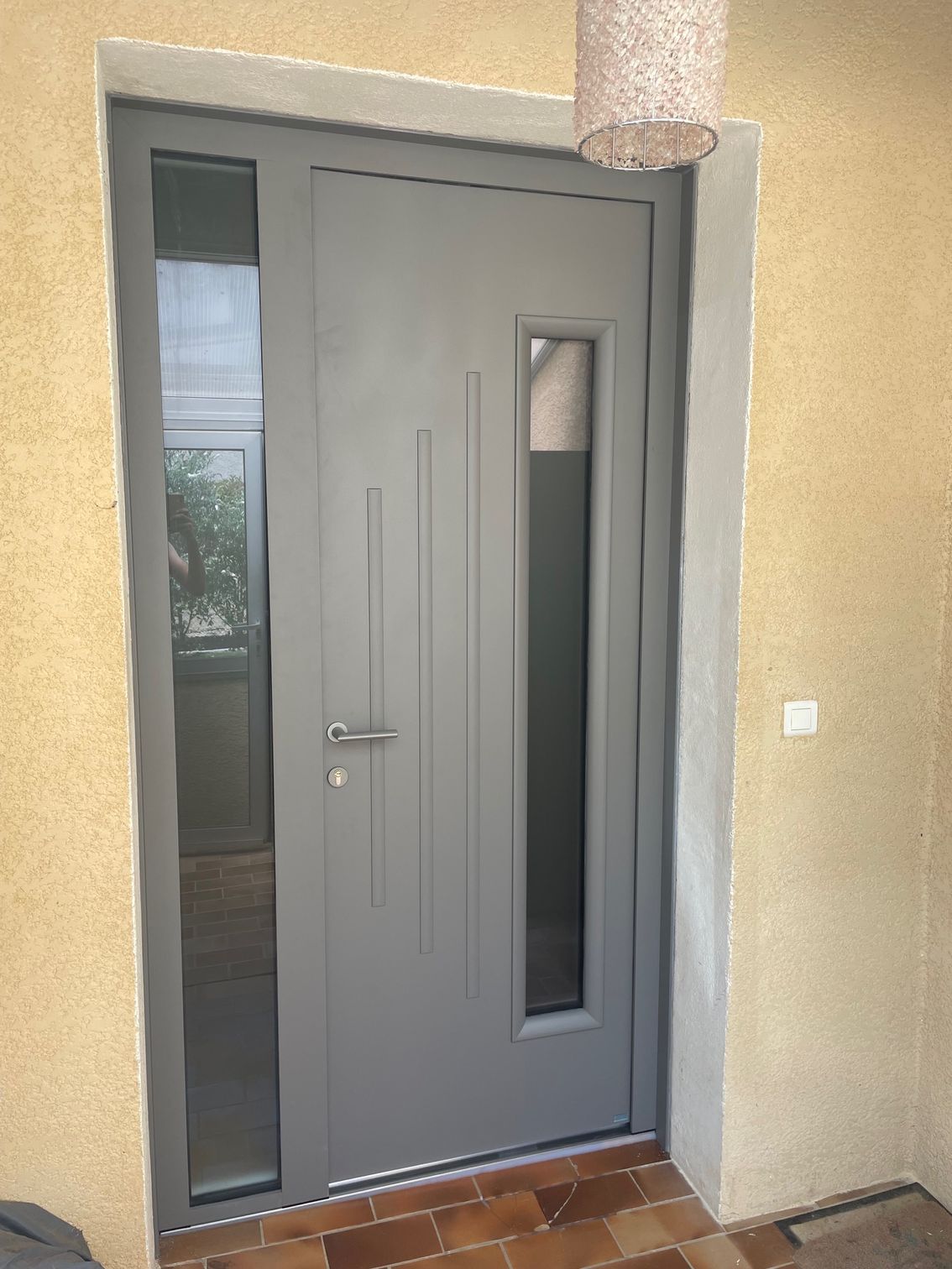 Porte d'entrée grise encadrée par des vitres