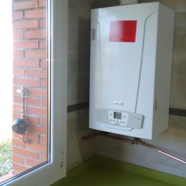 Una caldera blanca está colgada en la pared al lado de una ventana.