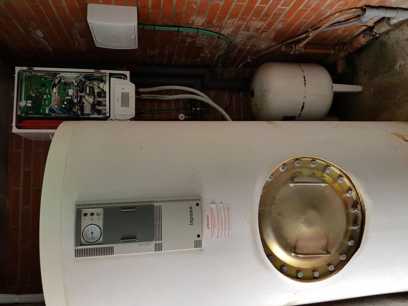 Un calentador de agua blanco está ubicado en una habitación al lado de una pared de ladrillos.