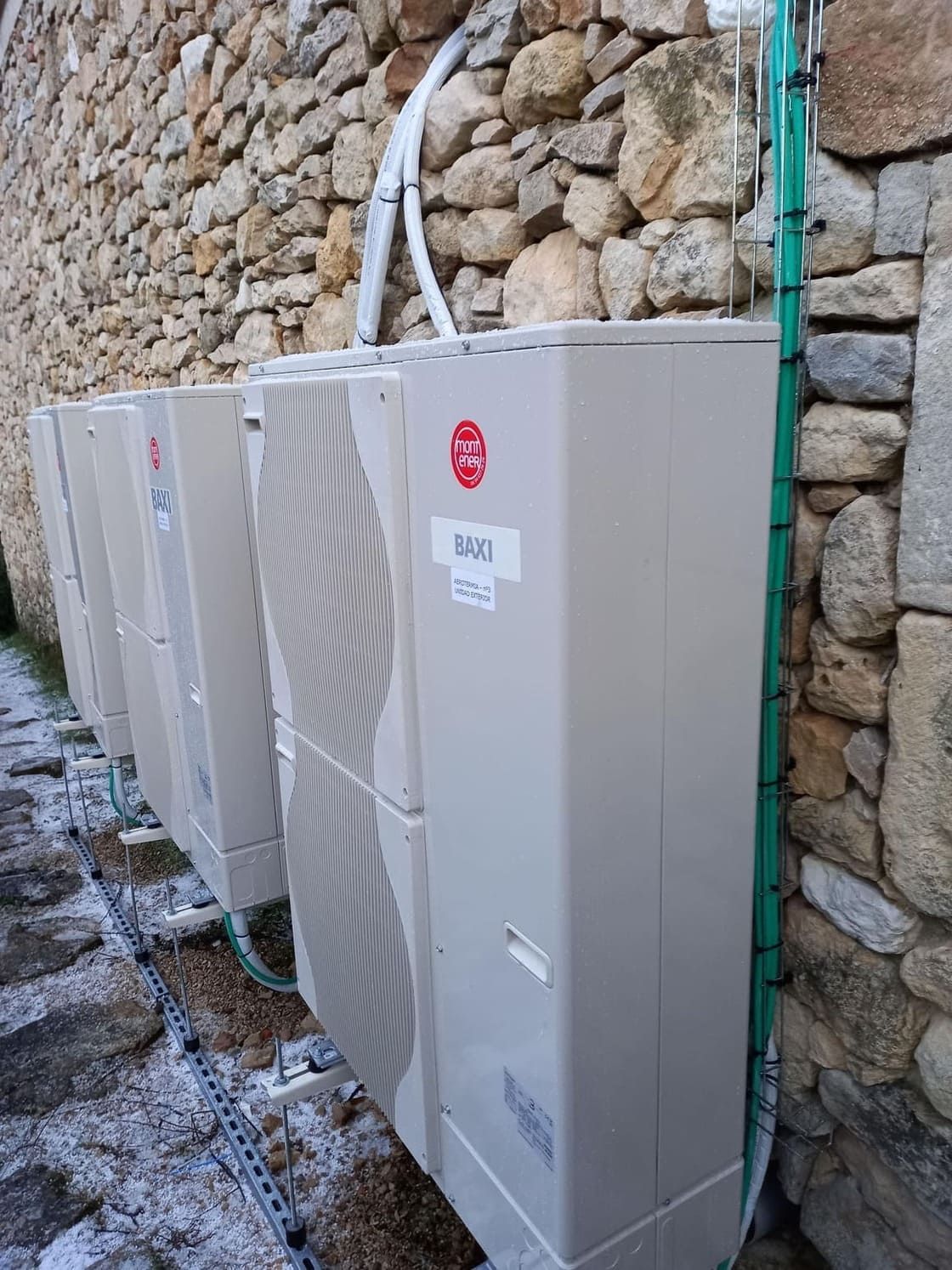 Una fila de aparatos de aire acondicionado junto a un muro de piedra.