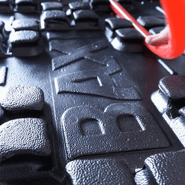 Una persona sostiene un objeto rojo sobre una alfombra de goma negra que dice