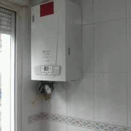 Una caldera blanca está colgada en la pared de una cocina, al lado de una ventana.