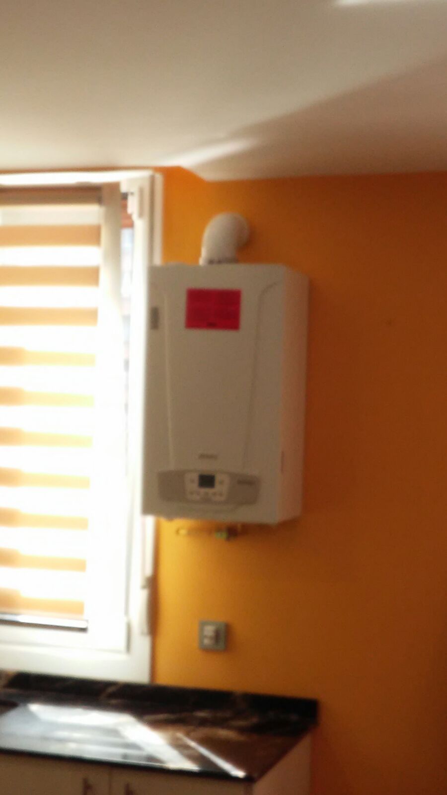 Una caja blanca con una pegatina roja está colgada en una pared al lado de una ventana.