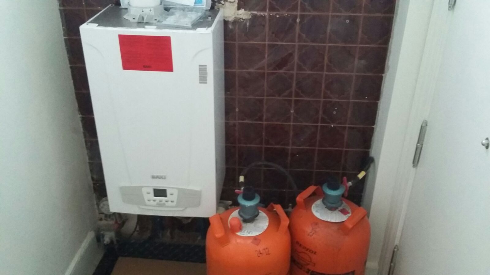 Hay dos bombonas de gas al lado de una caldera en una habitación.