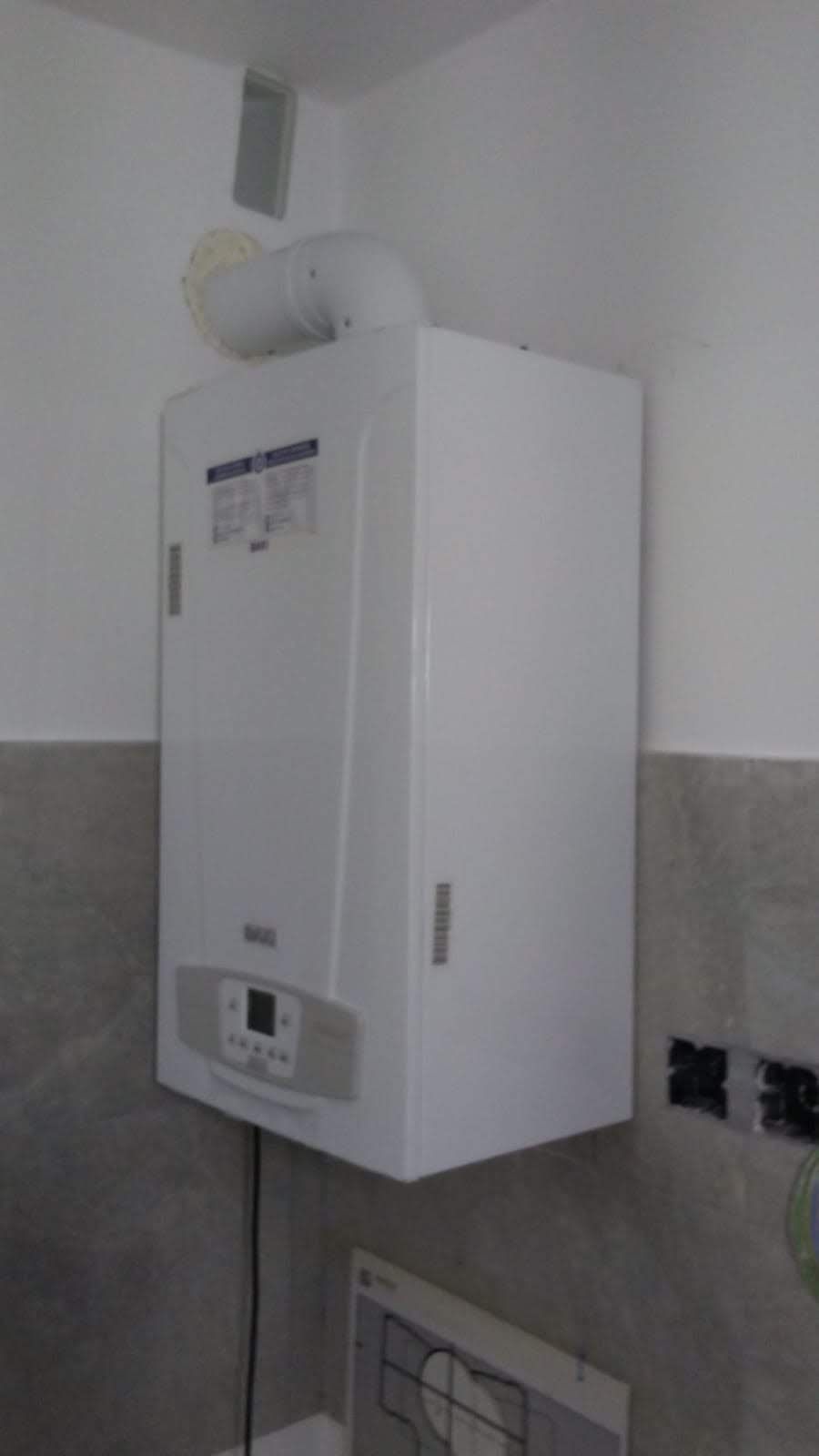 Una caldera blanca está colgada en la pared de un baño.