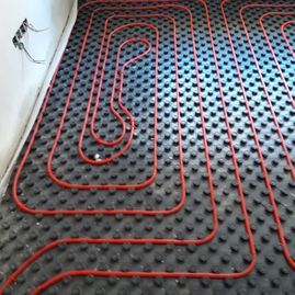 Un primer plano de un suelo radiante con tuberías rojas que lo atraviesan.