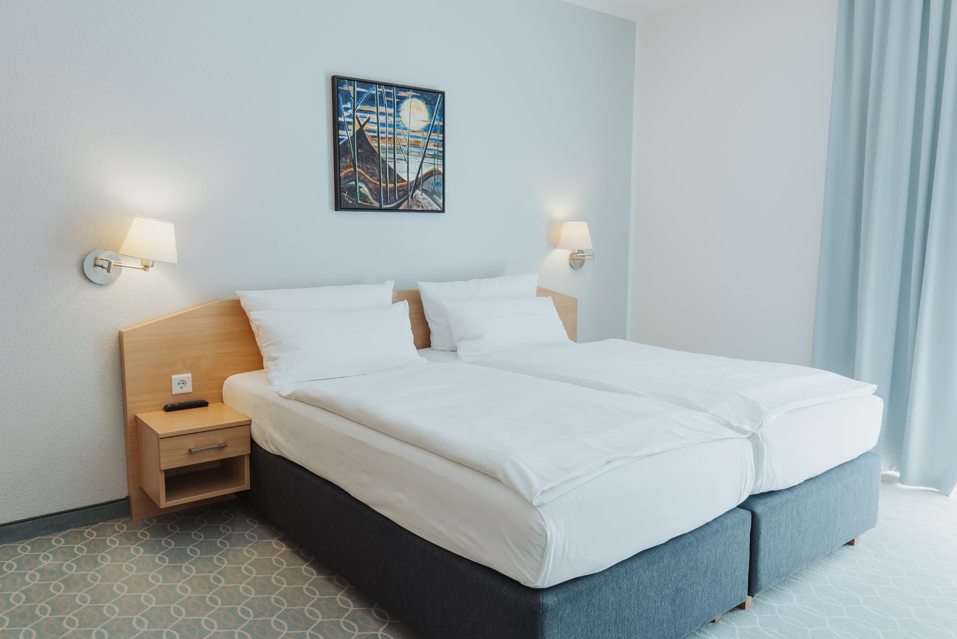 Zwei Frauen sitzen einander gegenüber auf einem Bett in einem warmen Hotelzimmer und unterhalten sich.