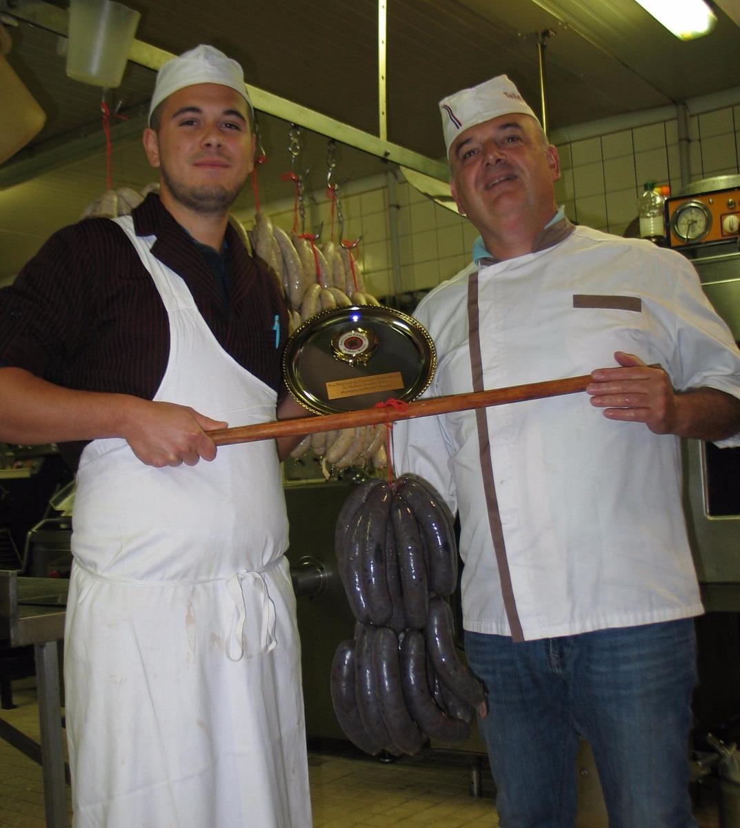 Deux hommes qui tiennent un prix et des boudins noirs qui pendent 