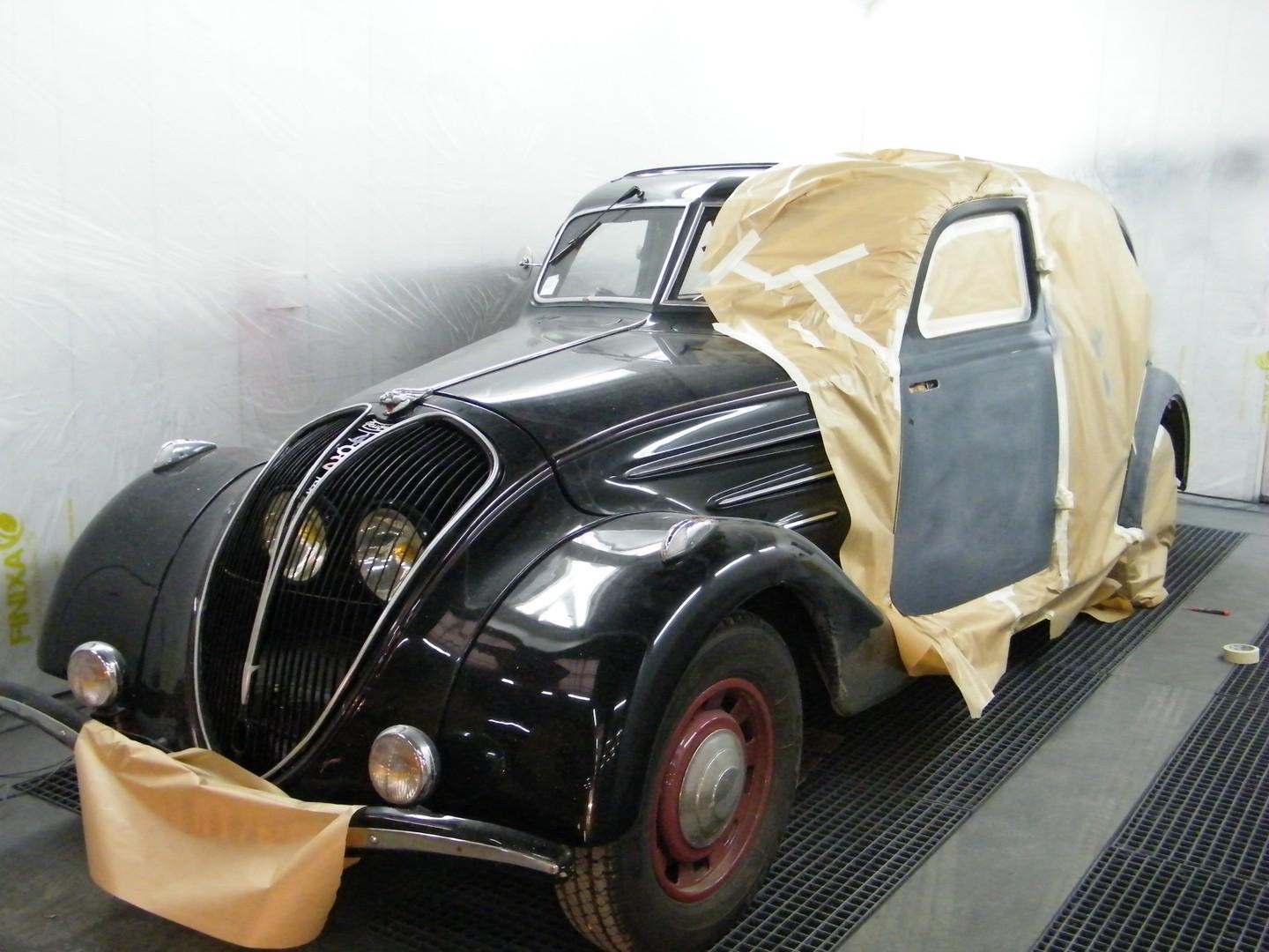 Vue sur une voiture ancienne en atelier, avec la porte avant gauche entourée d'une bâche pour appliquer la peinture.