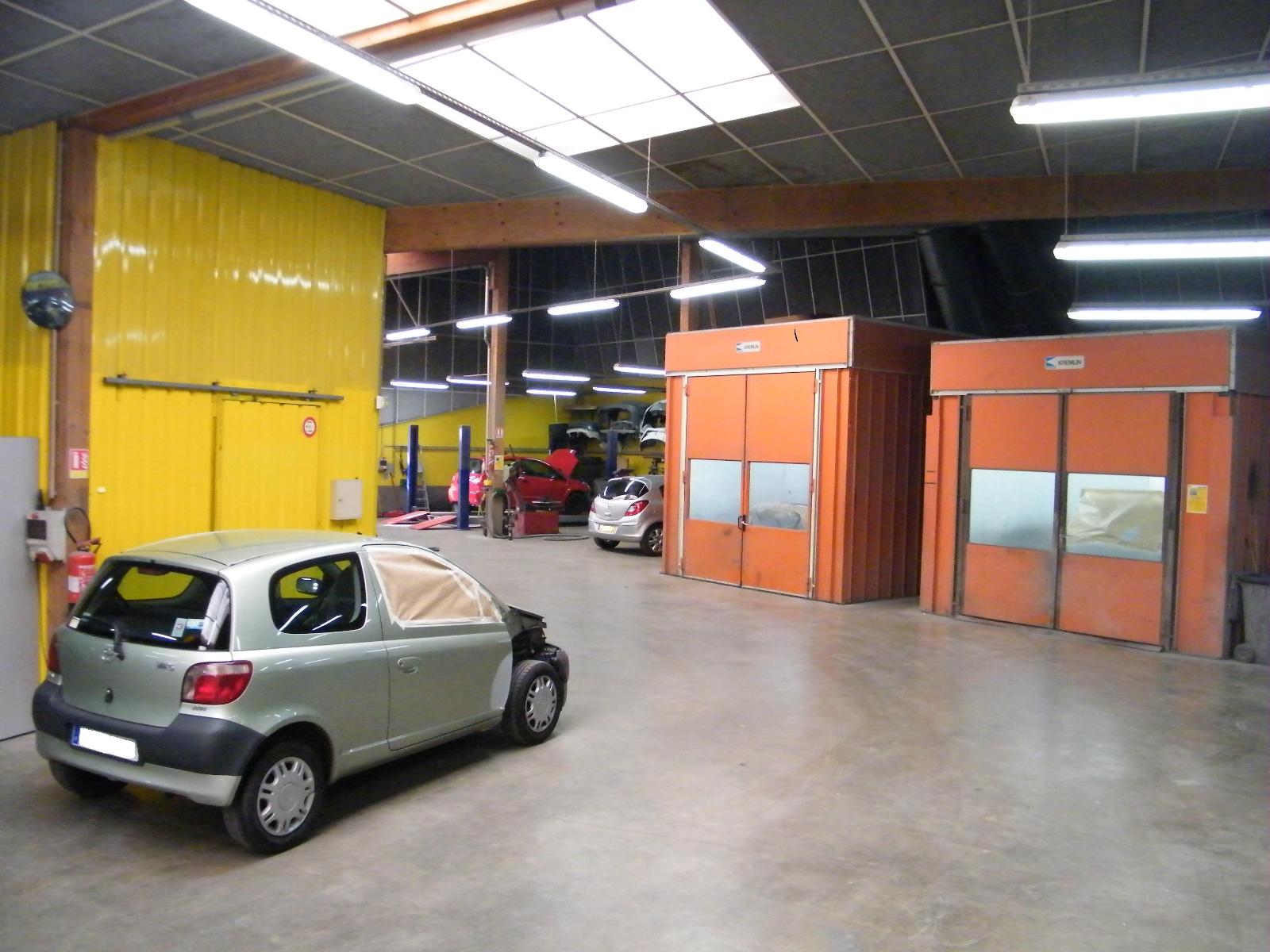 Intérieur de la Carrosserie Colas avec les box de traitement des véhicules en peinture, et une voiture grise au premier plan.