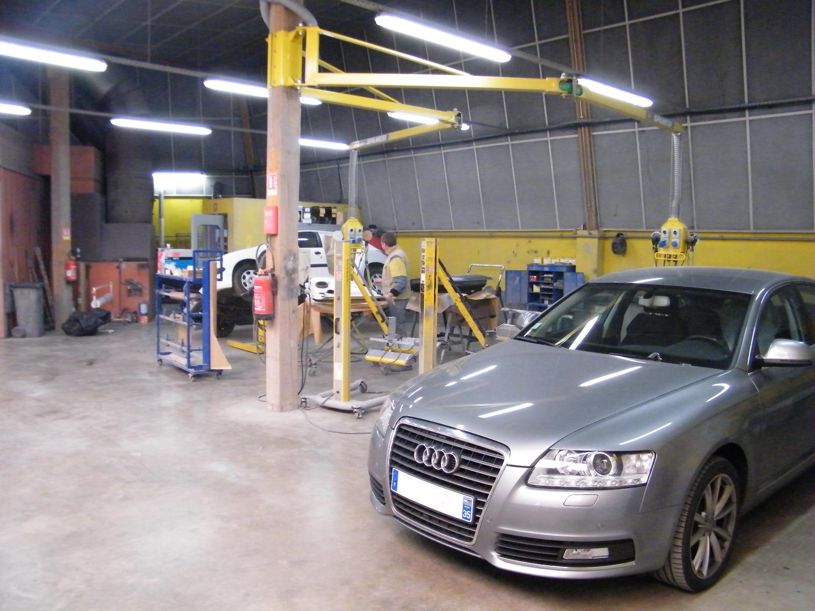 Atelier vu de l'intérieur de la Carrosserie Colas avec au fond une voiture en traitement, et devant une berline grise.