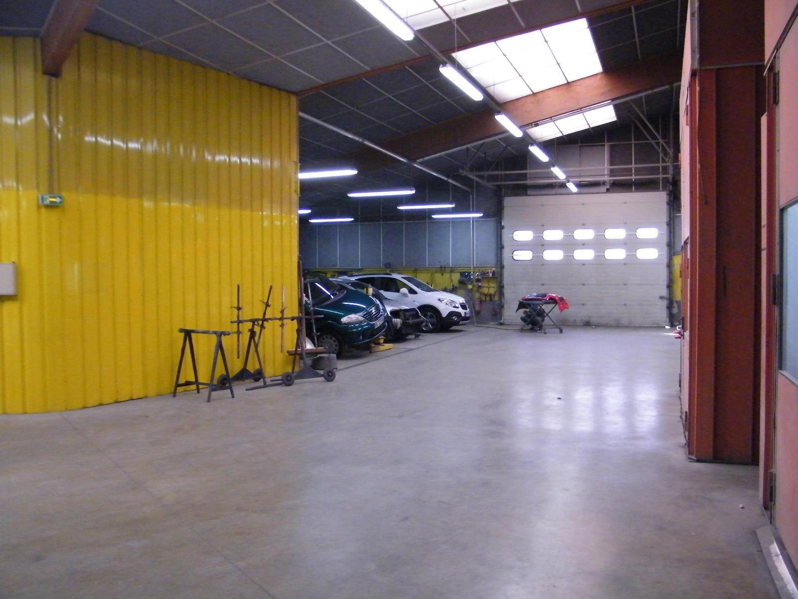Centre de l'atelier de la Carrosserie Colas avec le rideau fermé à l'entrée, et trois voitures en attente en haut à droite.