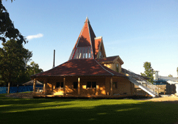 Holzgebäude mit großem, konischem Dach und Veranda auf einer Rasenfläche.