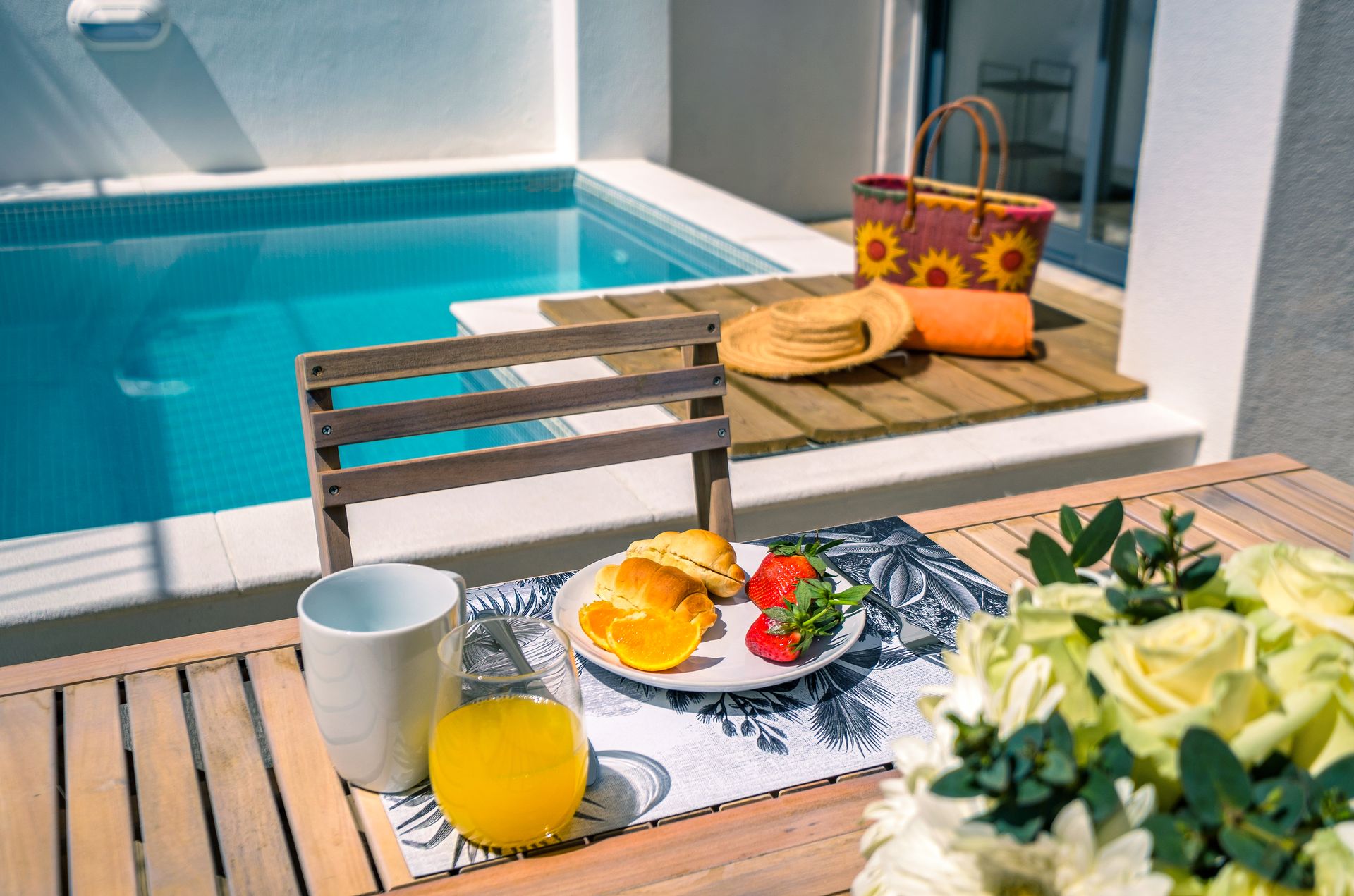 A table with a plate of food and orange juice next to a swimming pool.