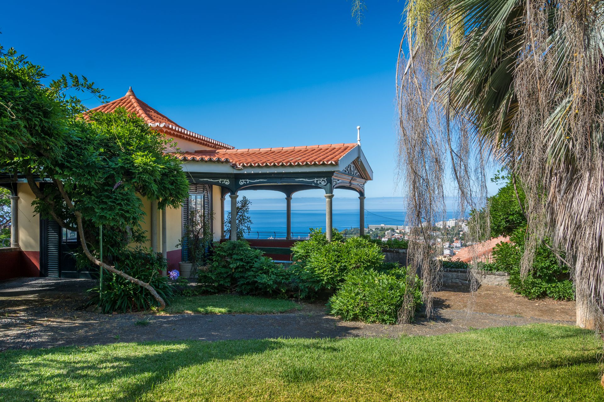 A house with a red tile roof is surrounded by trees and a lush green lawn.
