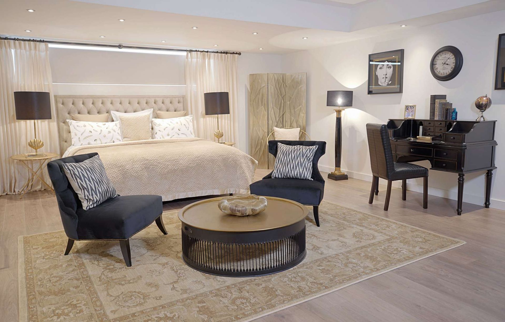 A bedroom with a king size bed , chairs , a coffee table and a desk.