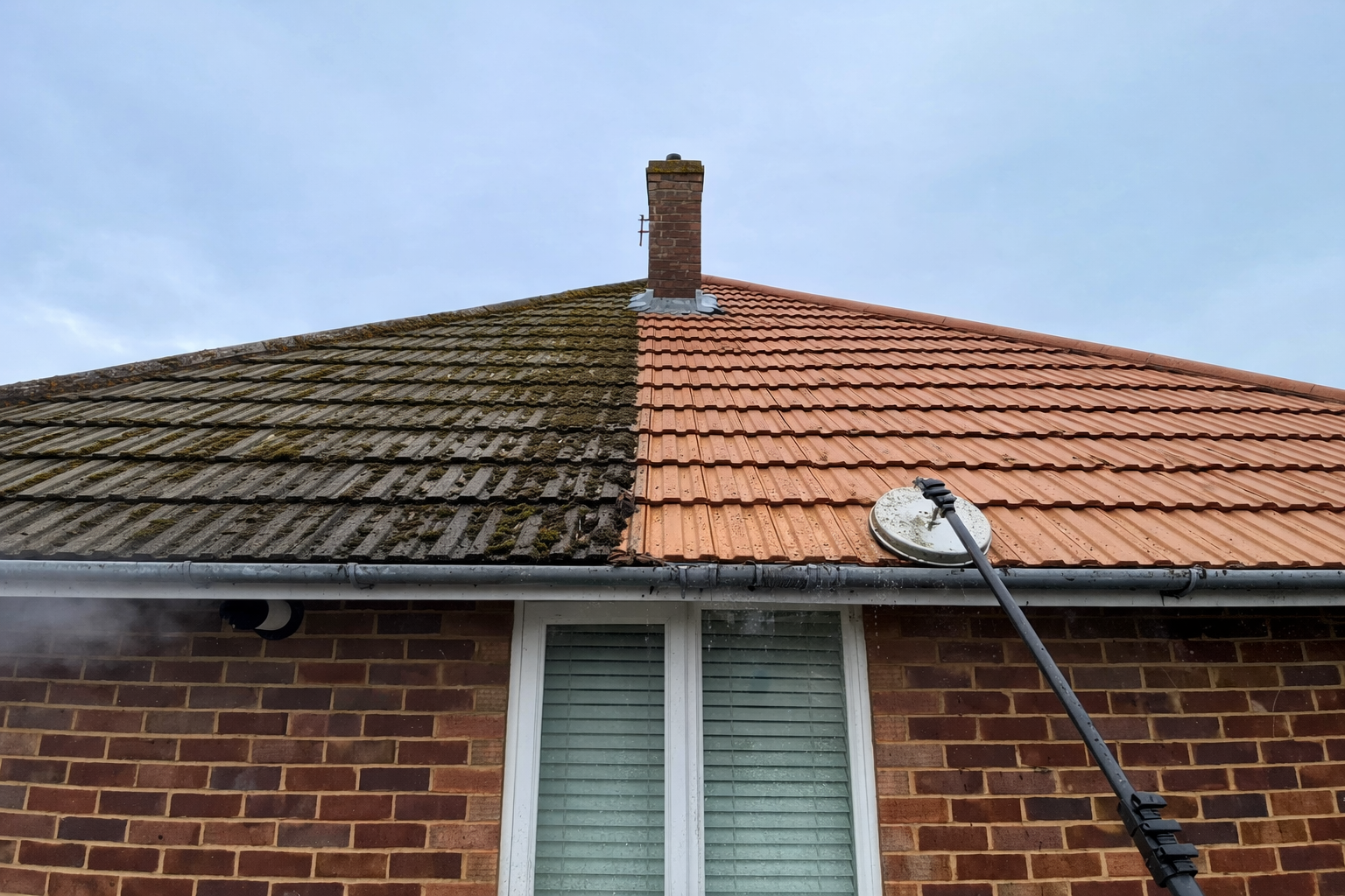 Partially reroofed brick house with dark old tiles and new orange tiles under a blue sky