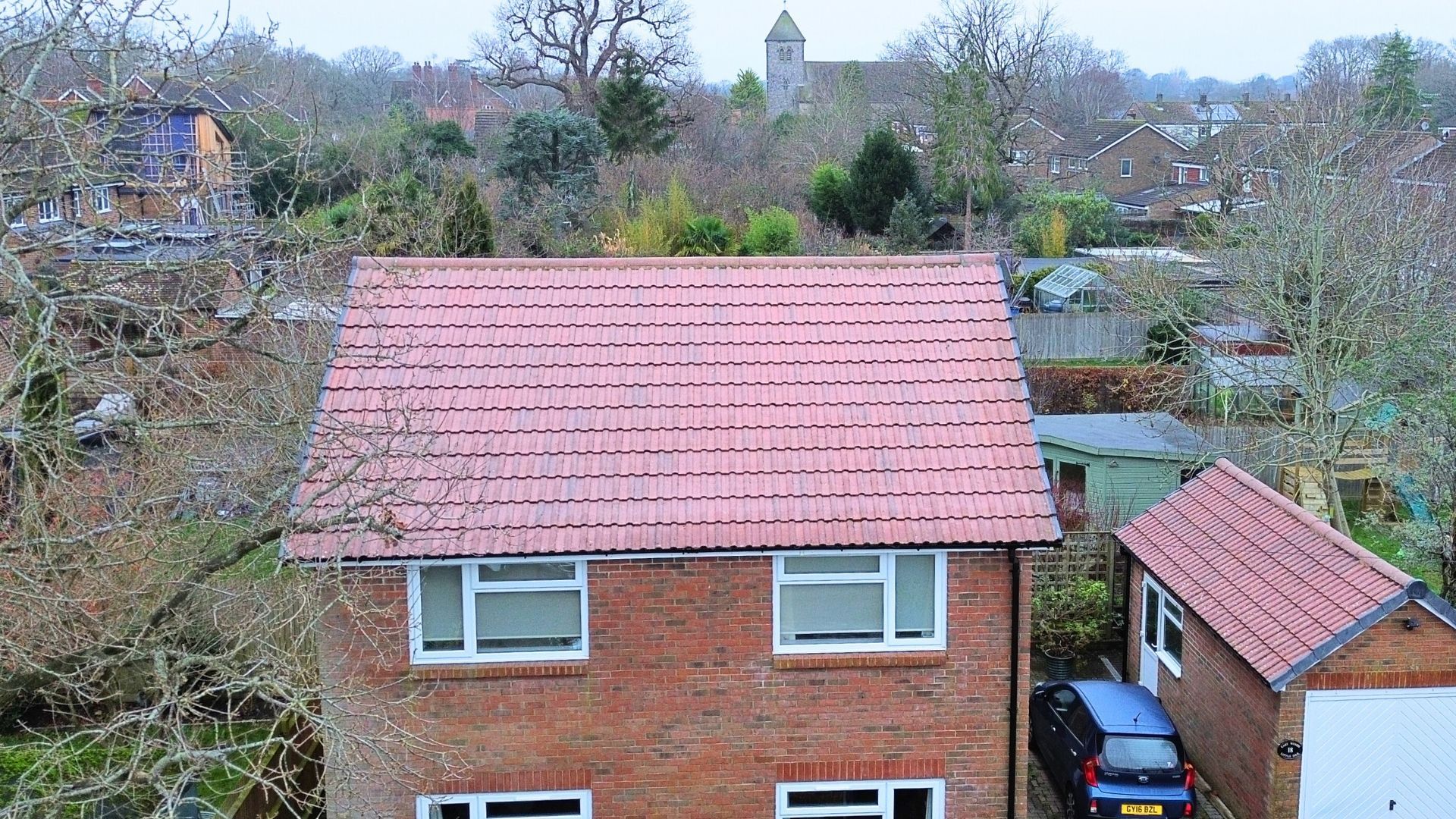 Suburban houses with red-tiled roofs and bare winter trees under an overcast sky