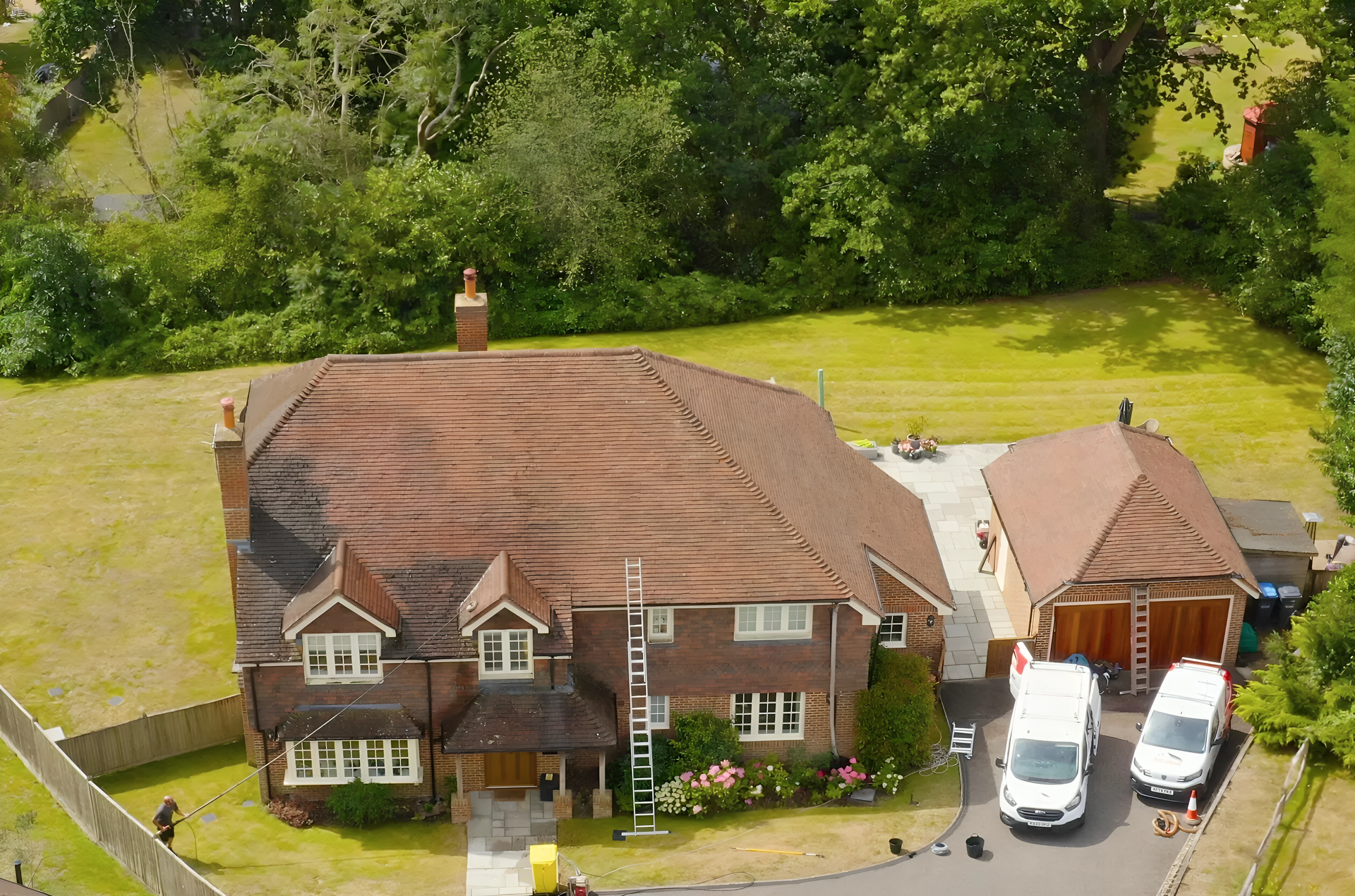 Aerial view of a suburban house with a brown roof, attached garage, and two white vans in the driveway.