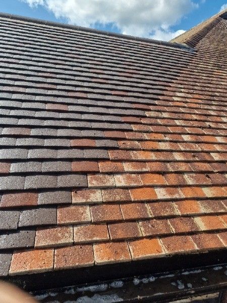 Close-up of a sloped roof with weathered red and gray shingles under a blue sky.