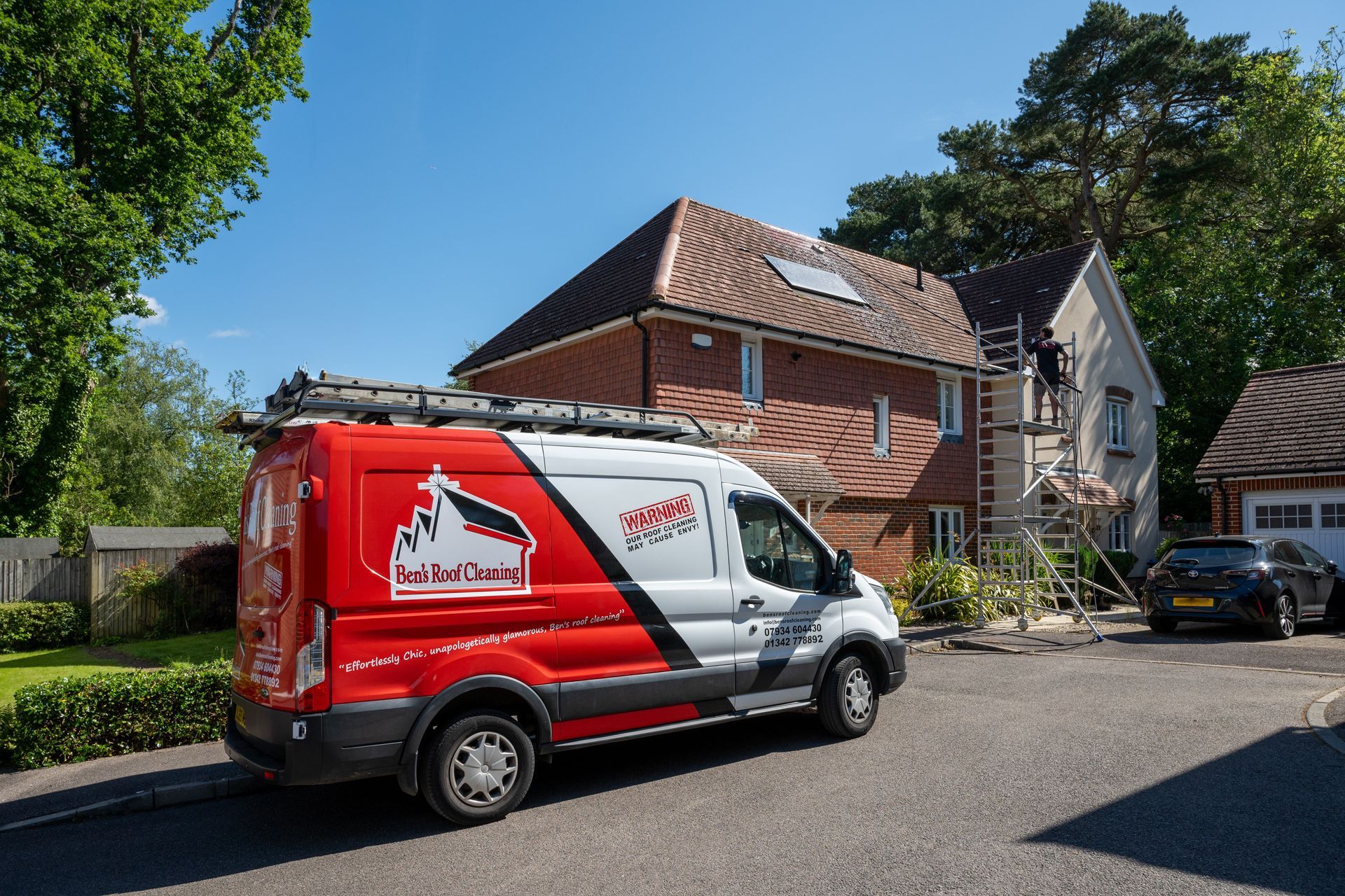 Red-and-white delivery van parked on a residential street beside a brick house.