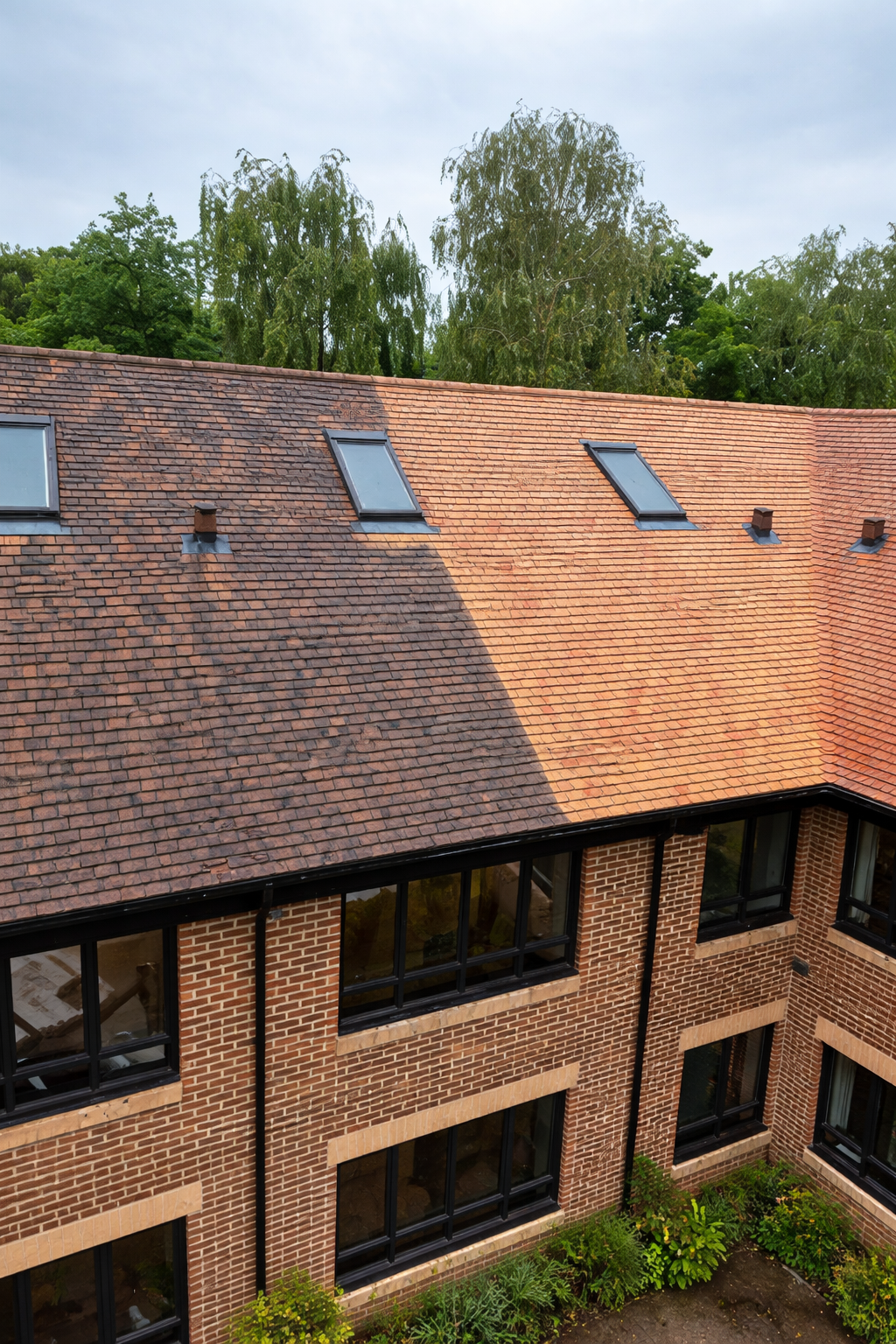 Brick building with a sloped red-tile roof and skylights, viewed from above under a partly cloudy sky