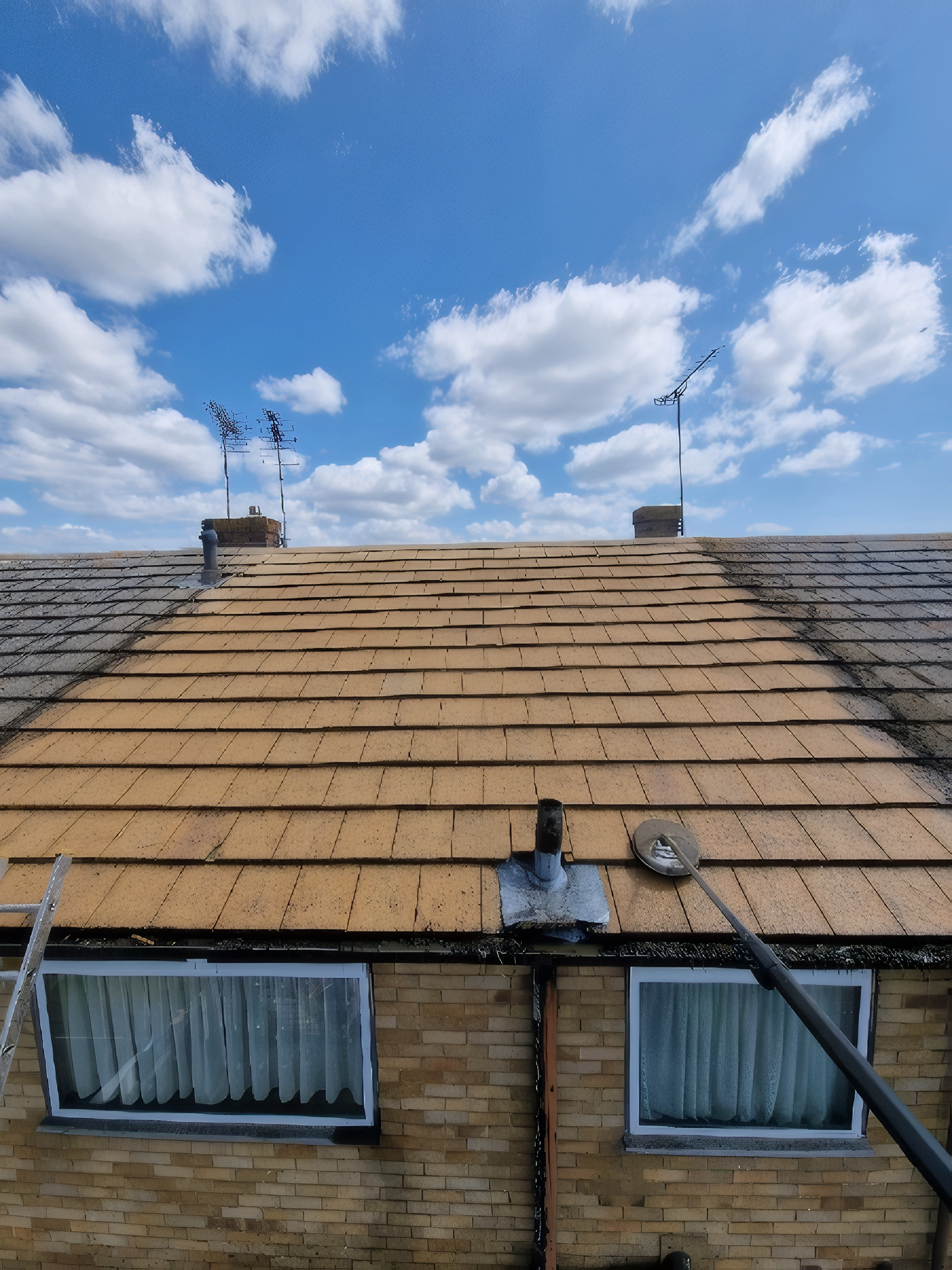Roof under repair with exposed underlayment, two dormer windows, and a bright blue sky with clouds.