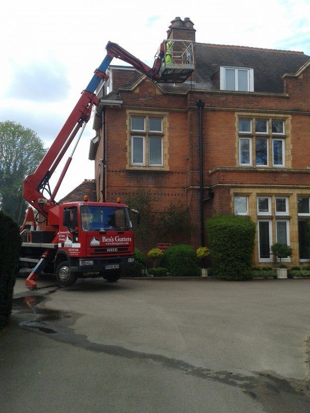 Red cherry picker lifting worker to roof of a brick townhouse