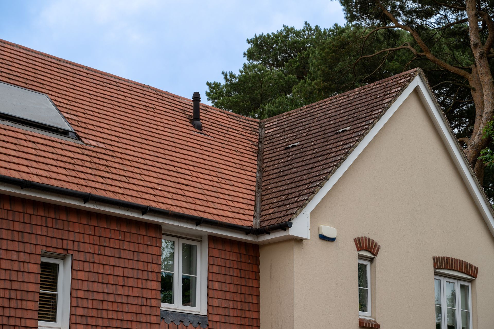 Red-tiled house roof and beige exterior walls with windows under trees