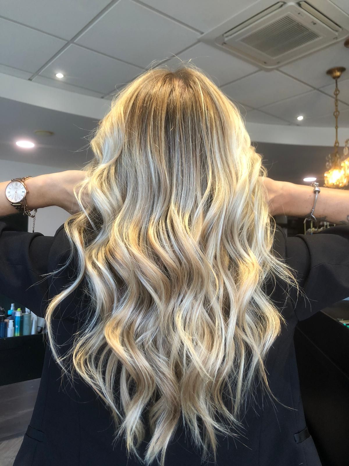 Femme aux cheveux ondulés blonds et châtain clair, les mains sur la tête, dans un salon de coiffure.
