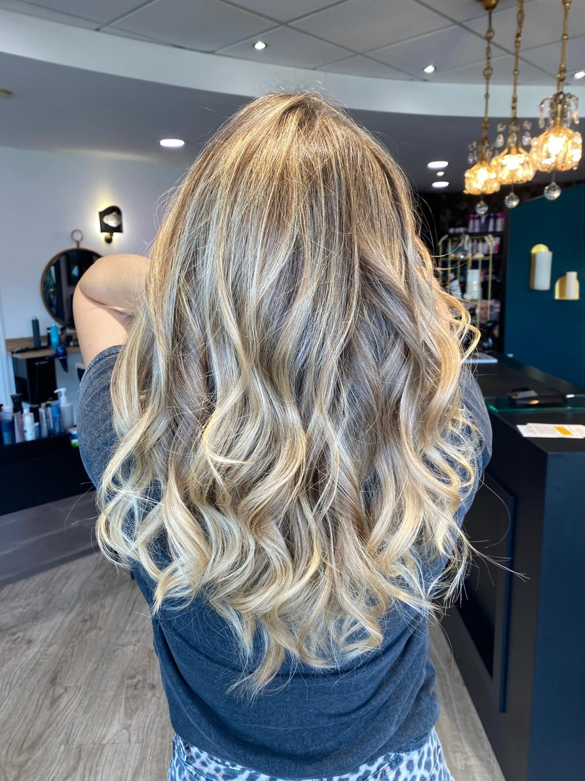 Femme aux cheveux ondulés blonds avec des mèches brunes dans un salon de coiffure.