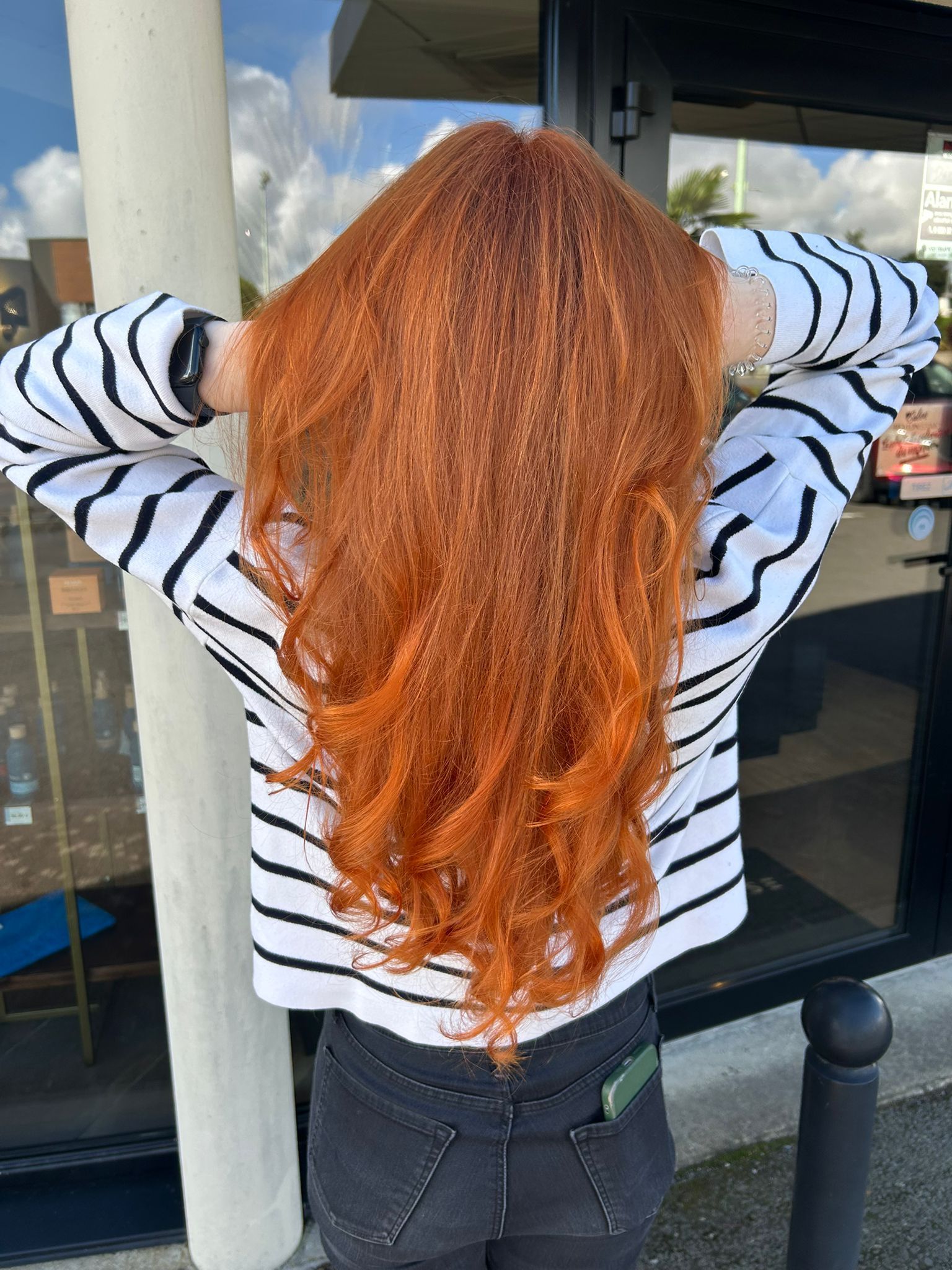 Personne aux longs cheveux roux et à la chemise rayée, les bras levés, debout à l'extérieur.