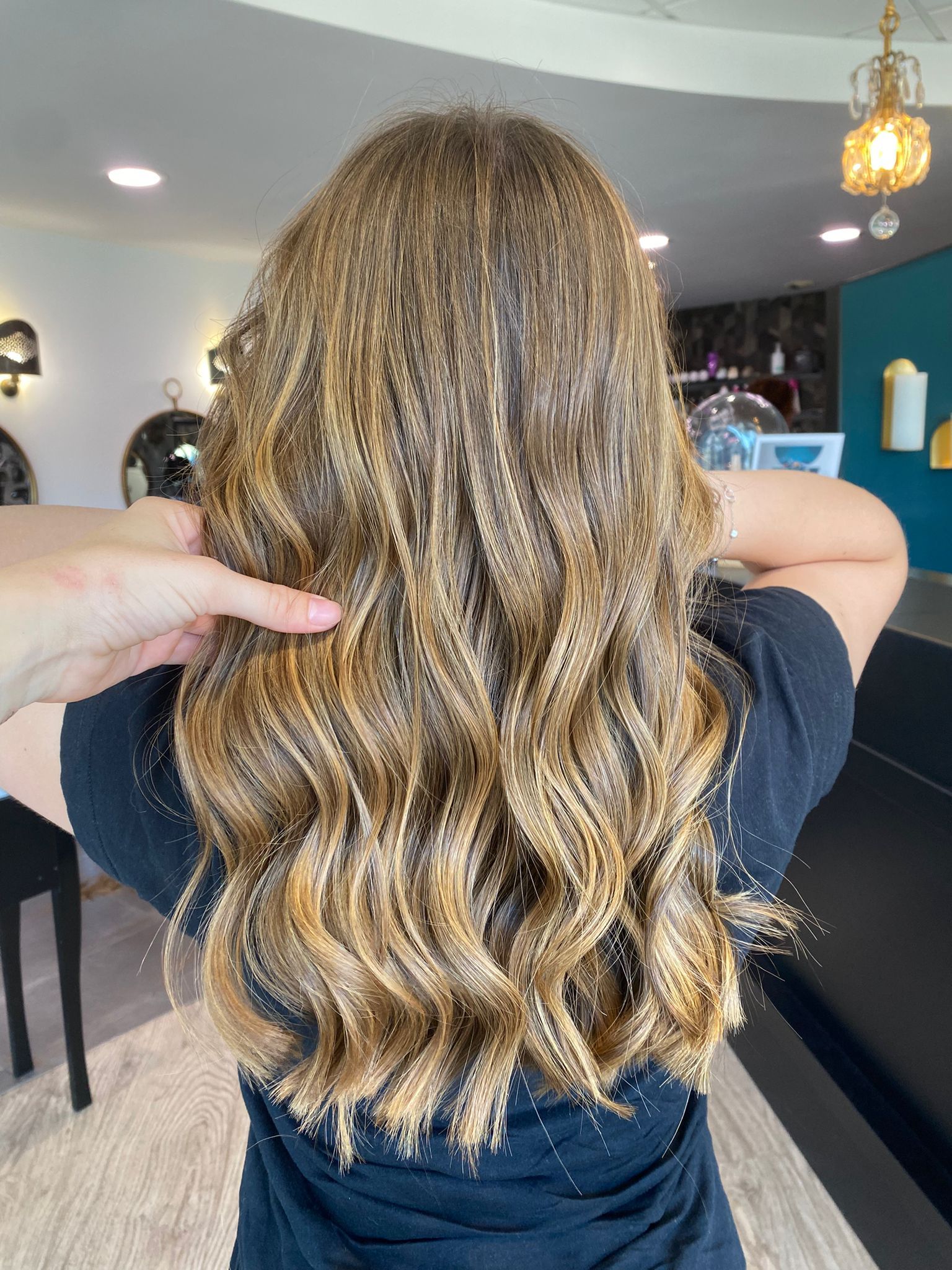 Femme aux cheveux bruns ondulés et méchés, dans un salon de coiffure.