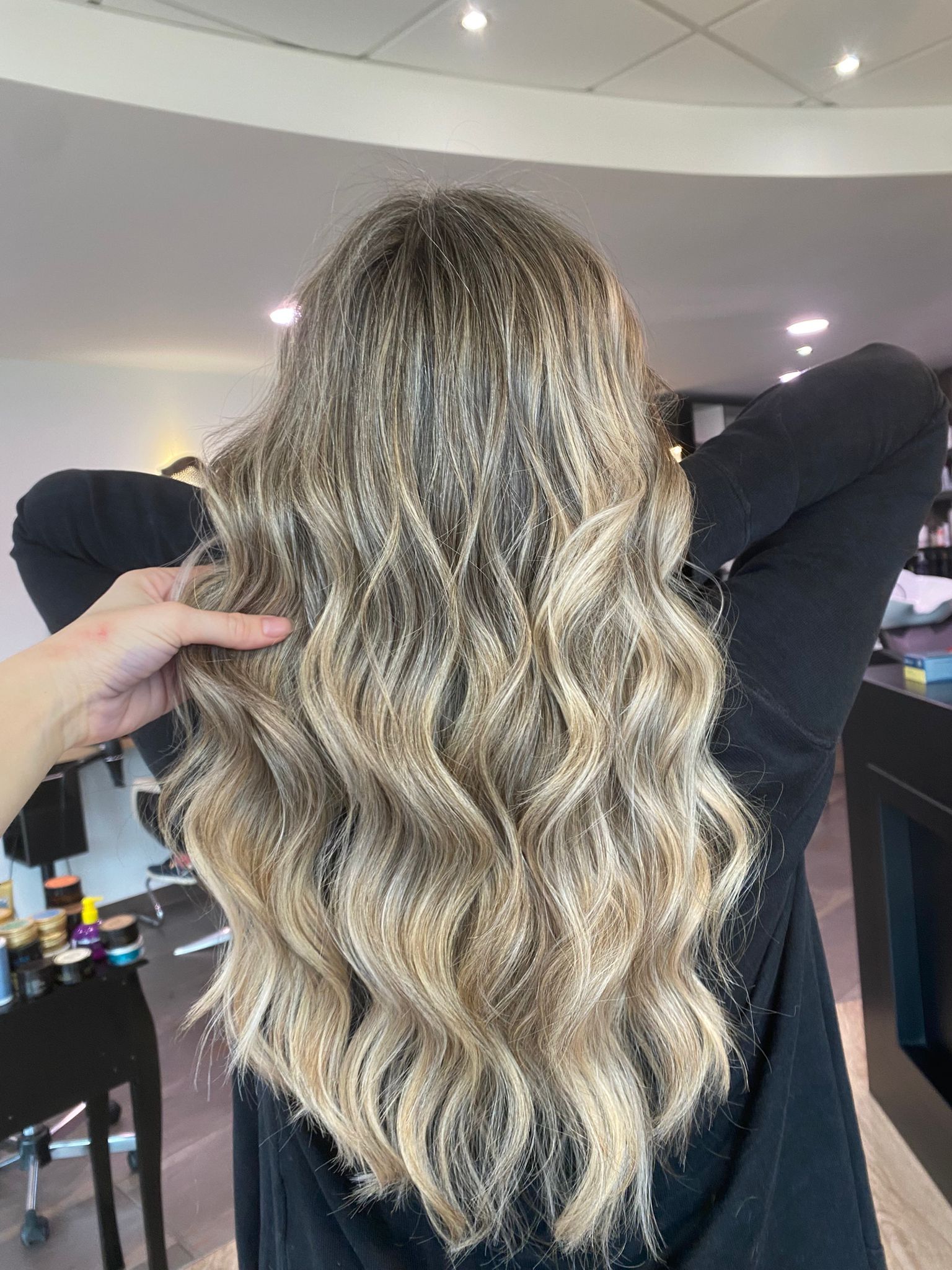 De longs cheveux blonds ondulés, coiffés en salon, avec une personne tenant une mèche.