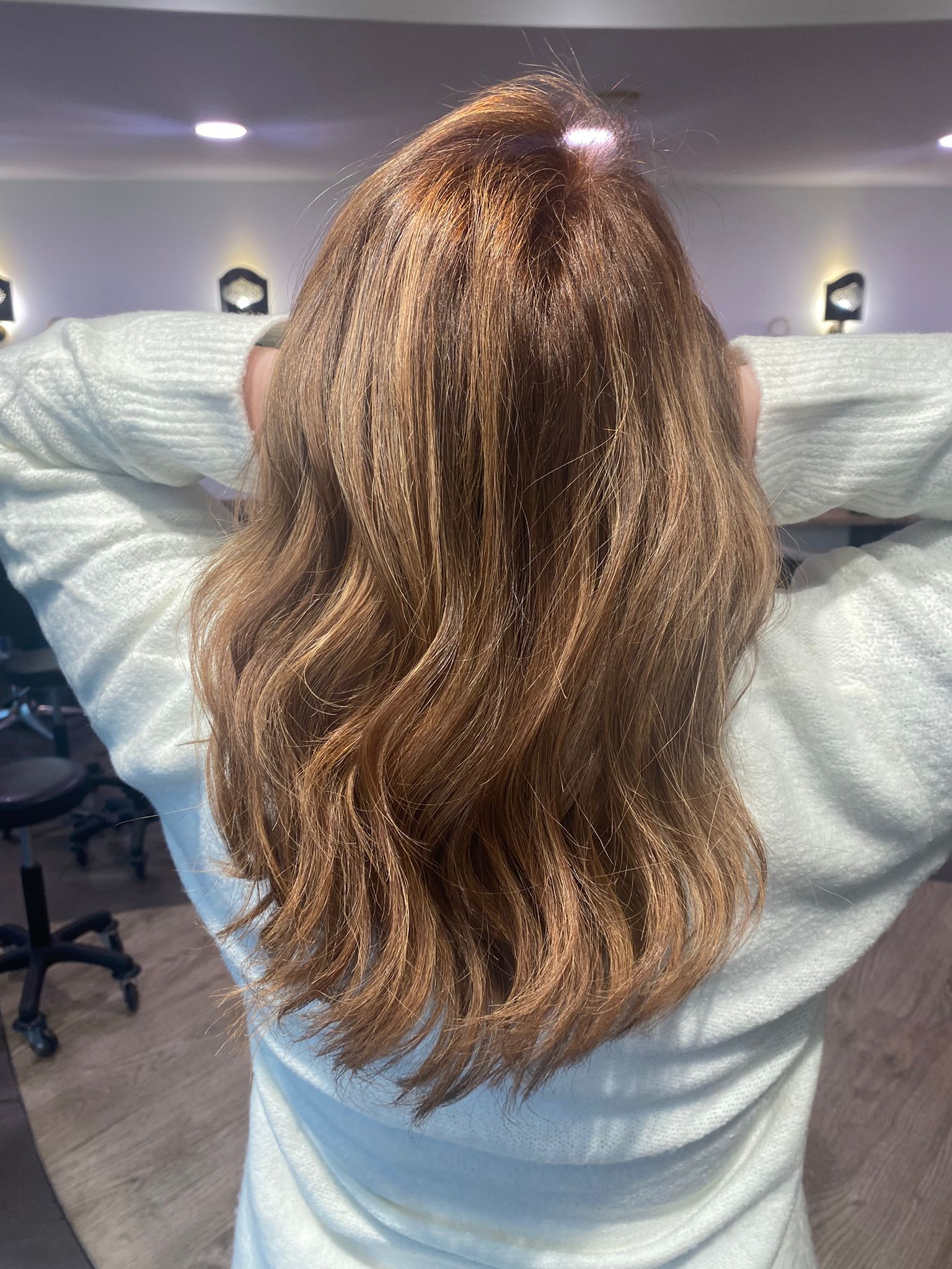 Personne aux longs cheveux bruns ondulés avec des reflets roux, vue de dos, les bras levés.