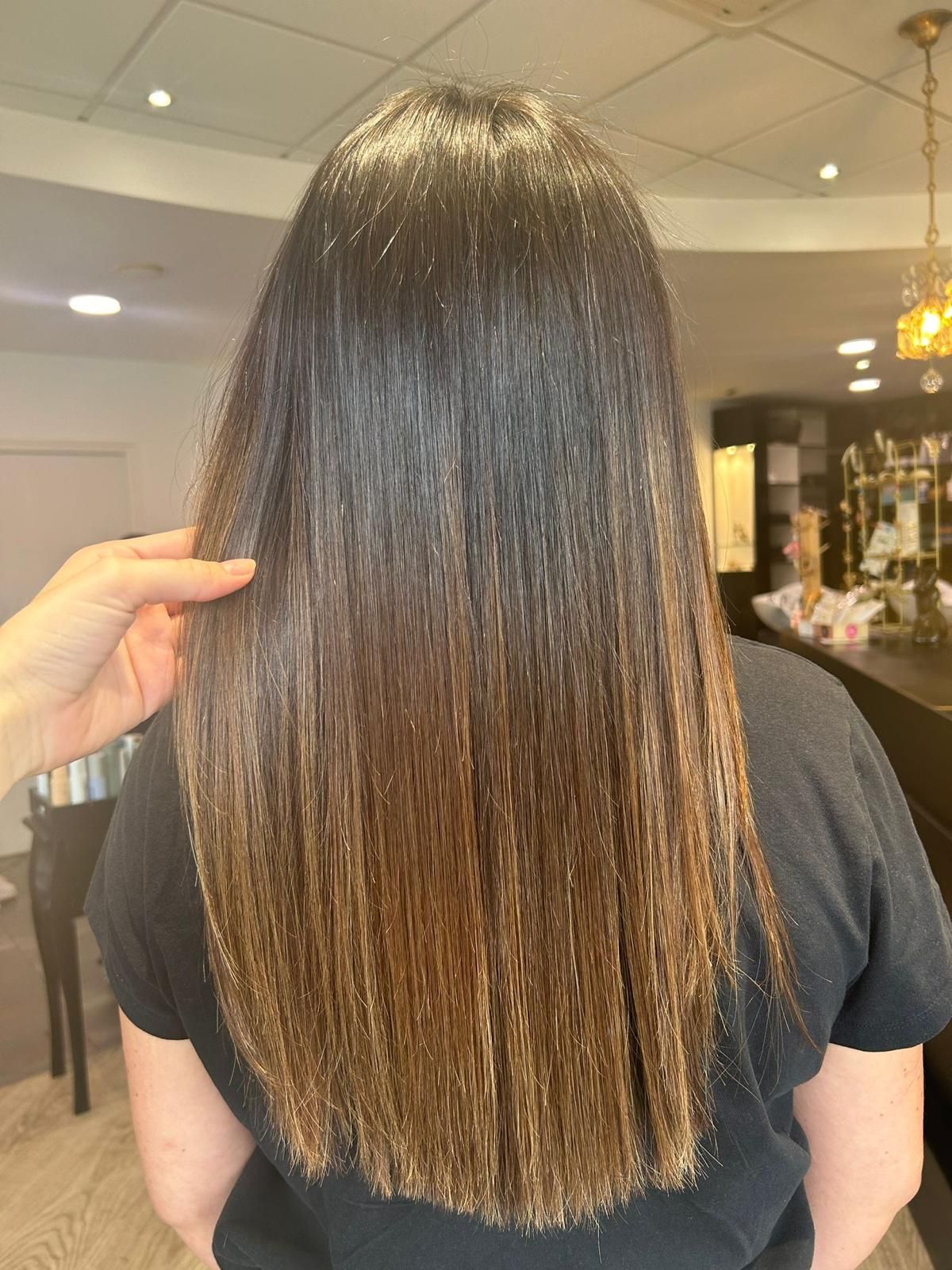 Une personne aux cheveux lisses et ombrés se trouve dans un salon de coiffure ; sa main touche ses cheveux.