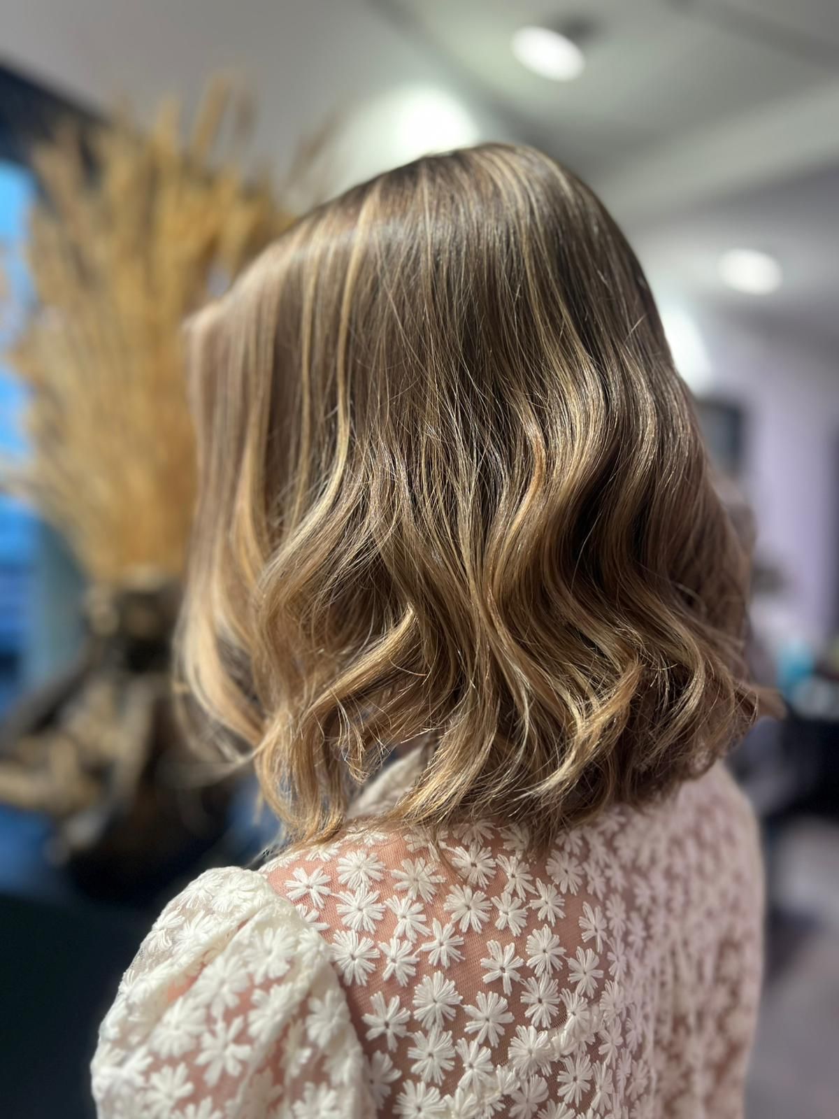 Cheveux blonds ondulés mi-longs avec de subtils reflets, coiffés en salon.