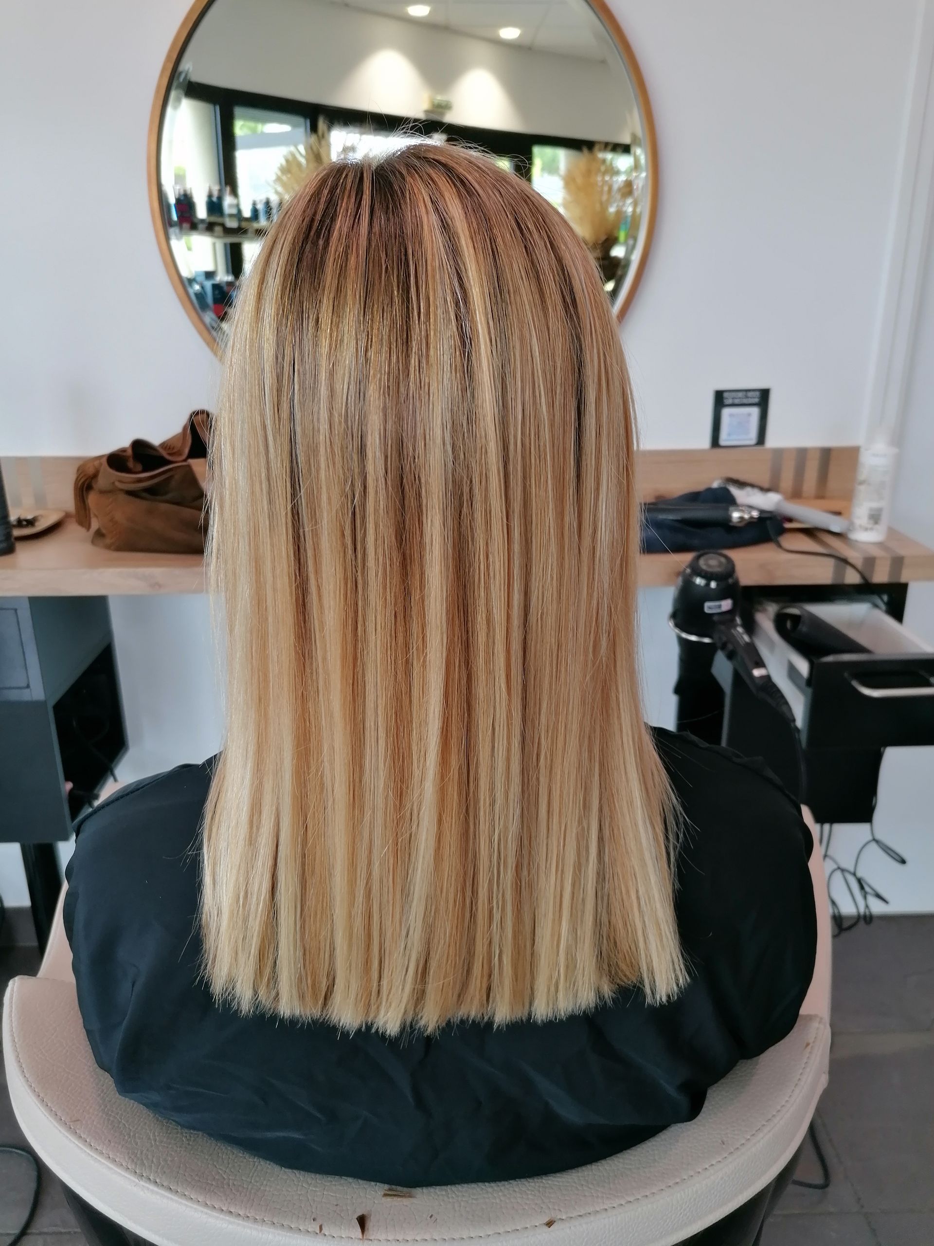 Cheveux blonds lissés en salon avec une texture crêpée aux racines.