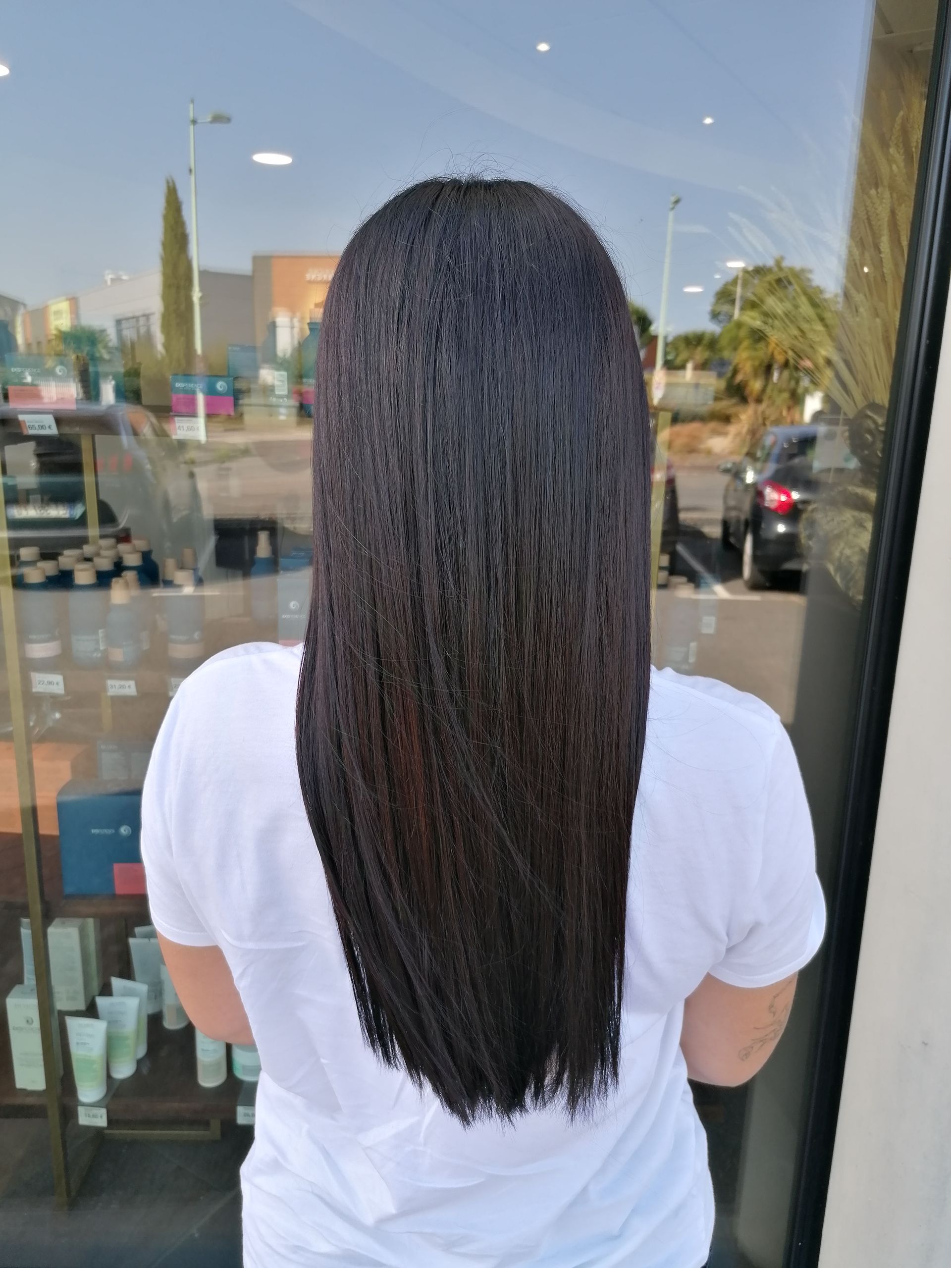Personne aux longs cheveux foncés, tressés en micro-tresses, portant une chemise blanche, debout devant une vitrine.