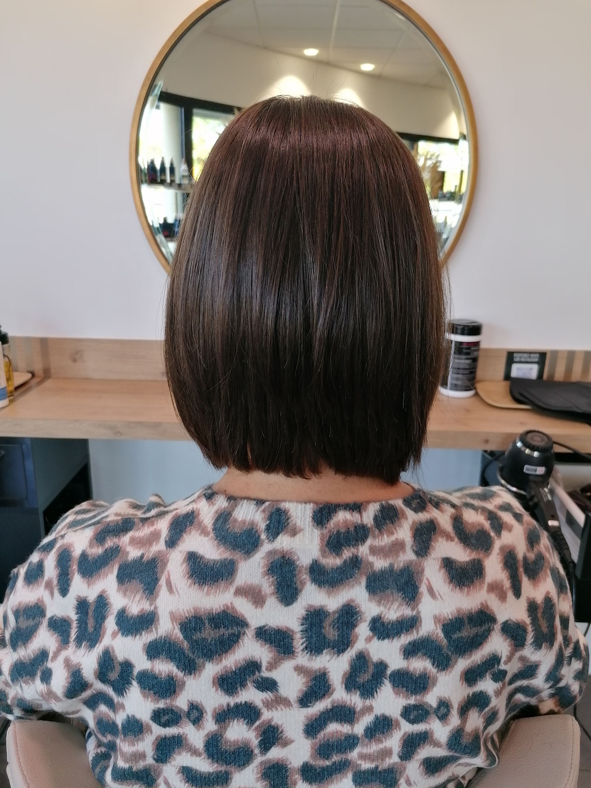 Femme aux cheveux brun foncé coupés au carré, portant un pull à motifs, dans un salon de coiffure.