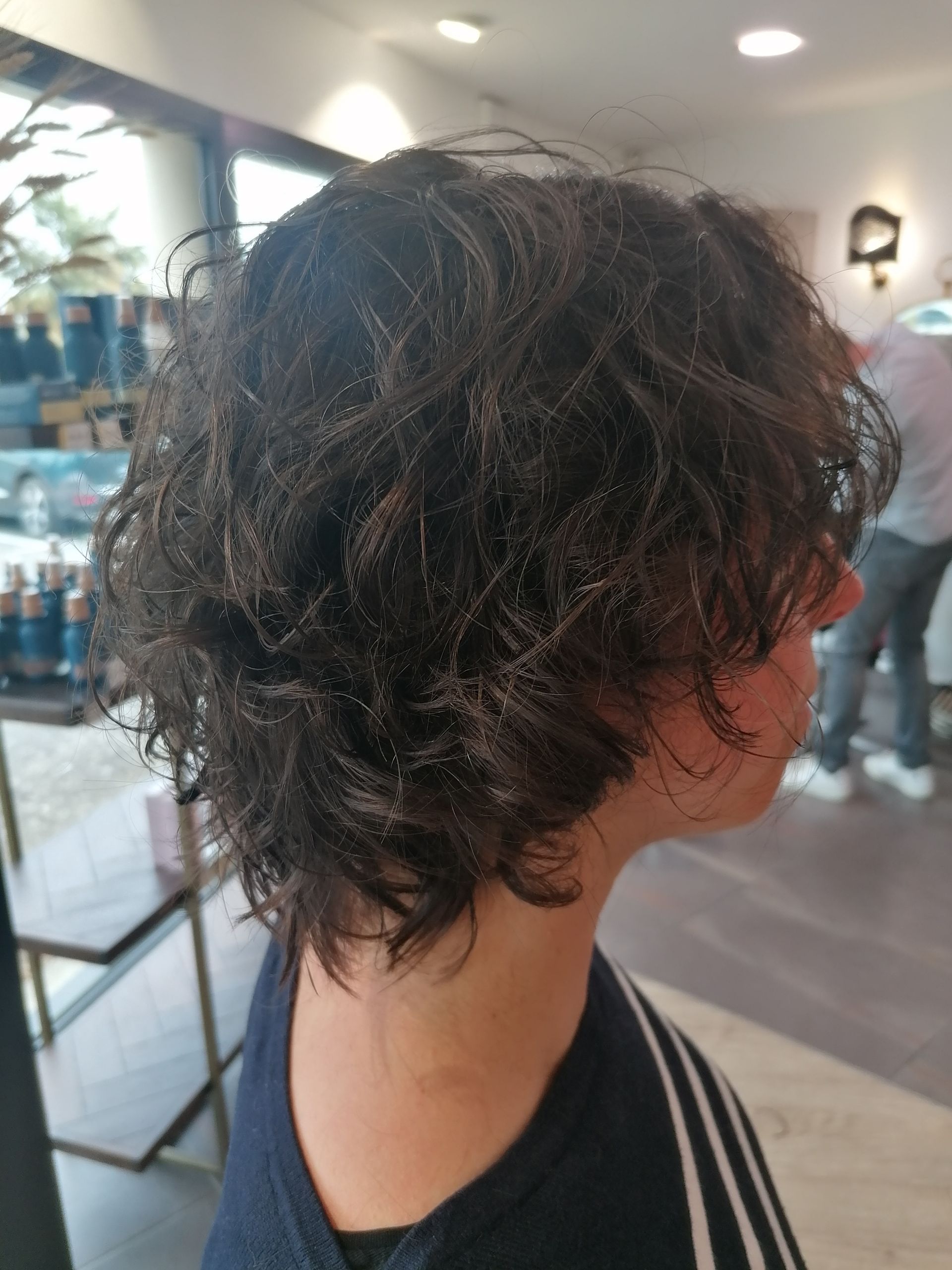 Femme aux cheveux foncés et bouclés dans un salon de coiffure, vue de profil.