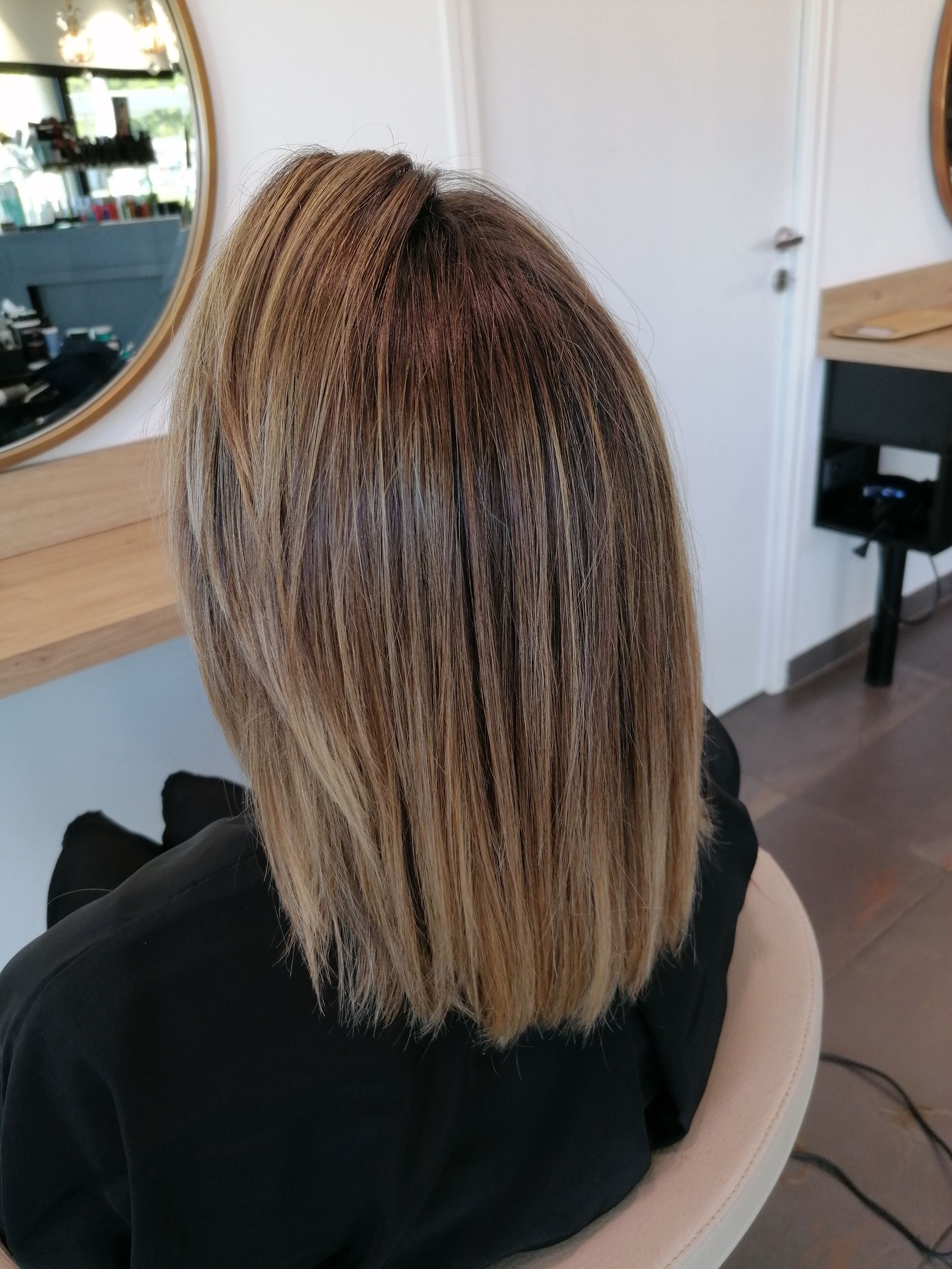 Femme aux cheveux lisses et méchés, assise sur un fauteuil de salon, dos à la caméra.