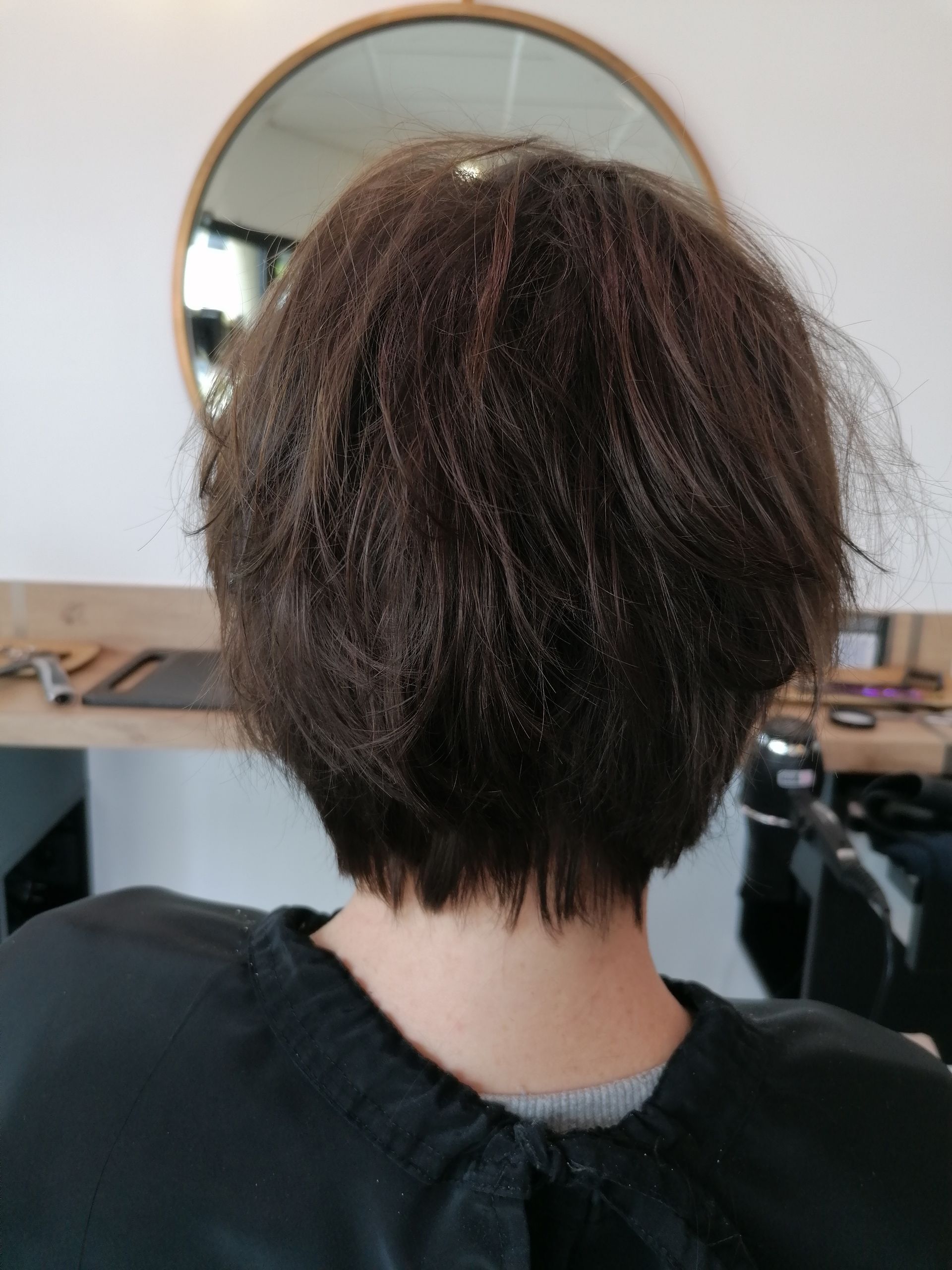 Personne aux cheveux foncés et texturés, coupe au carré court, de dos. De retour dans un salon de coiffure, devant un miroir.